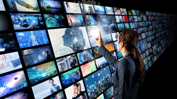 A woman looking at many screens and touching one of them.