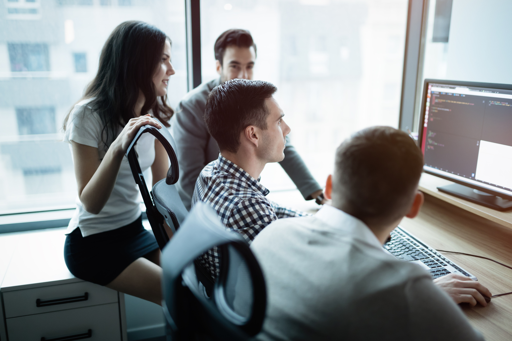 Business people sitting around a computer with code on the screen.