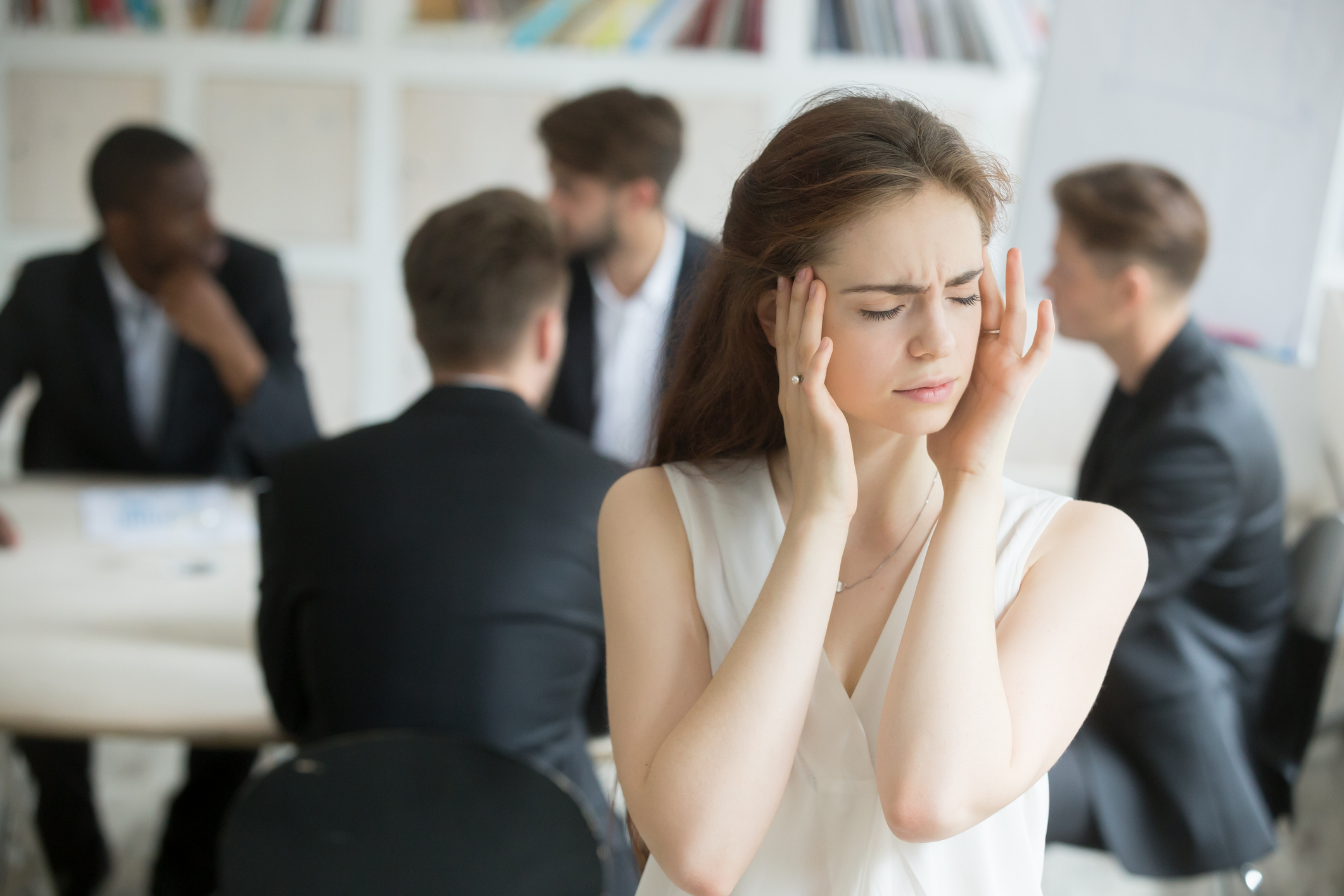 Woman plugging ears with fingers in front of table of men in suits