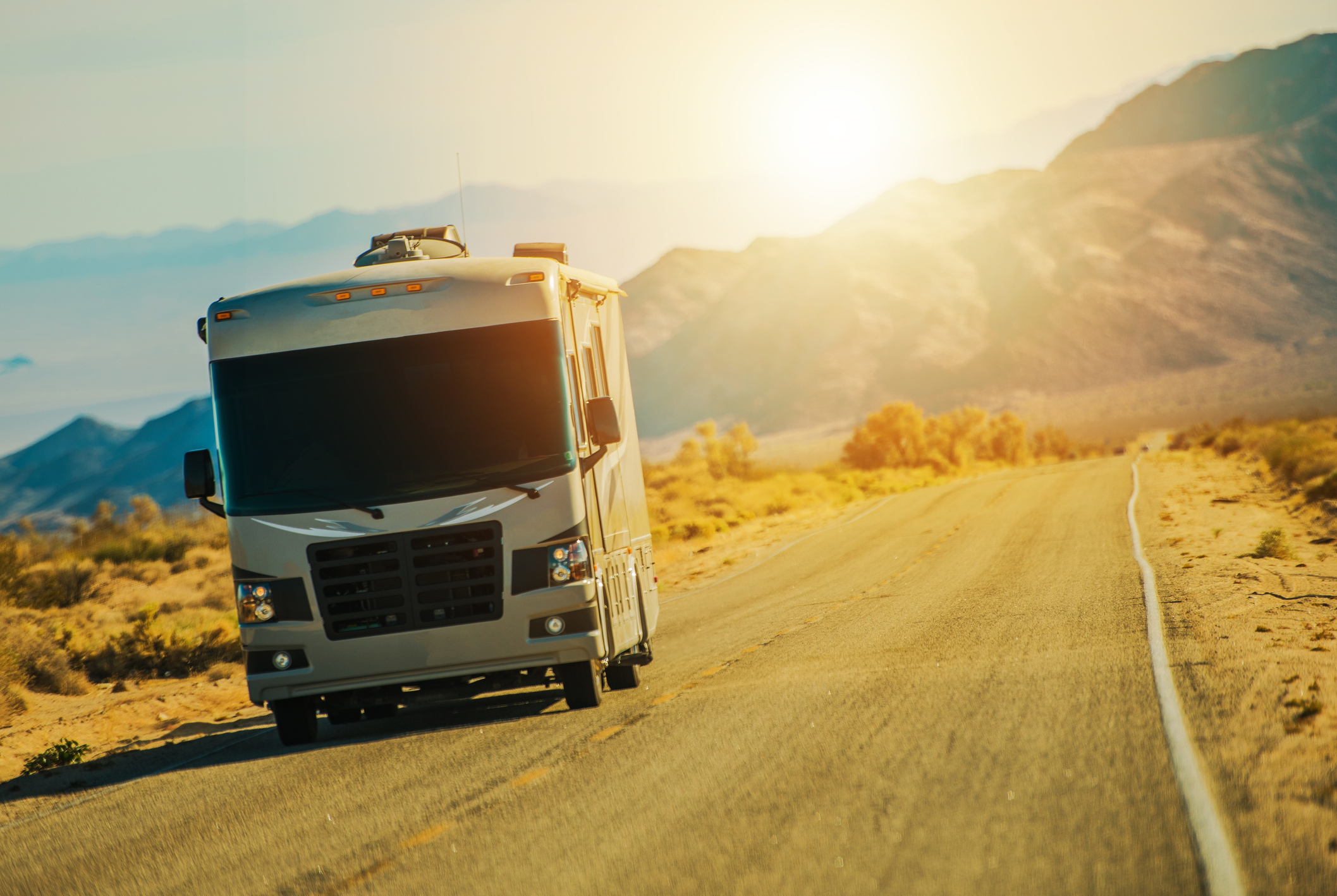An RV drives in front of a western sunset.