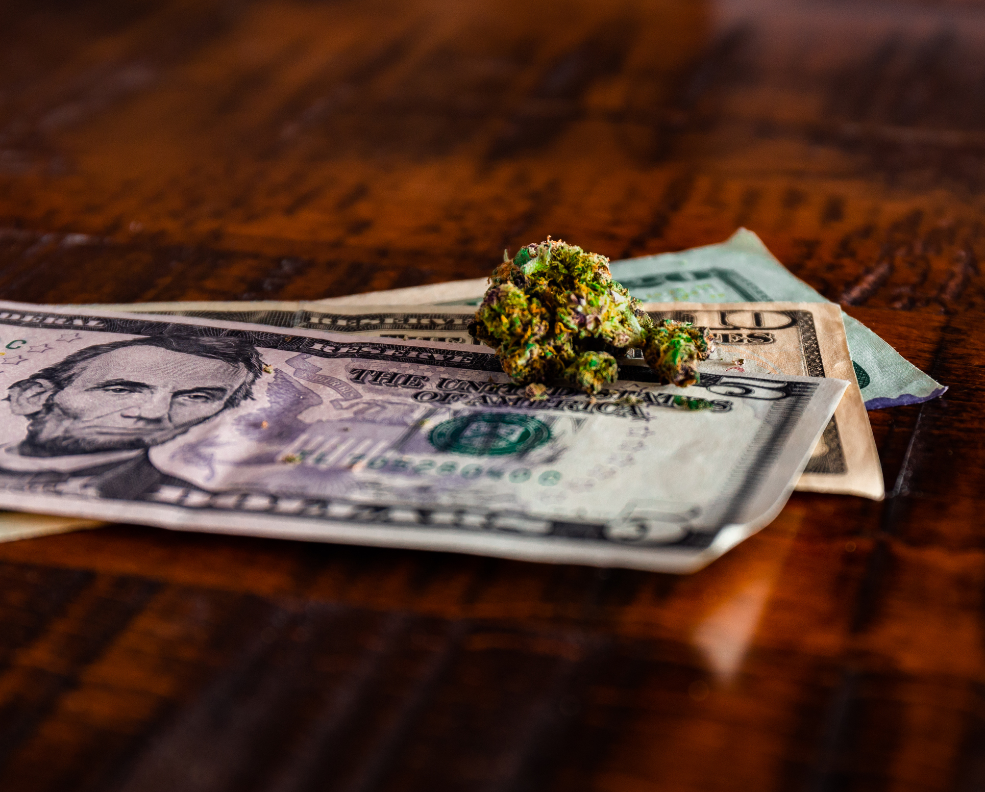 A cannabis bud sits atop a small pile of U.S. currency.