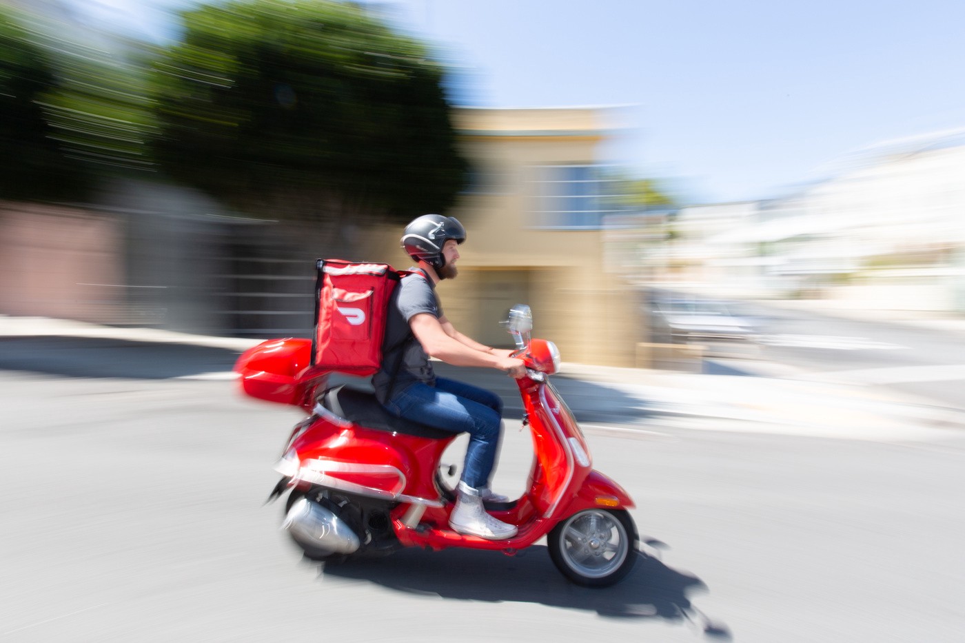 A DoorDash driver making a delivery on a red DoorDash scooter. 