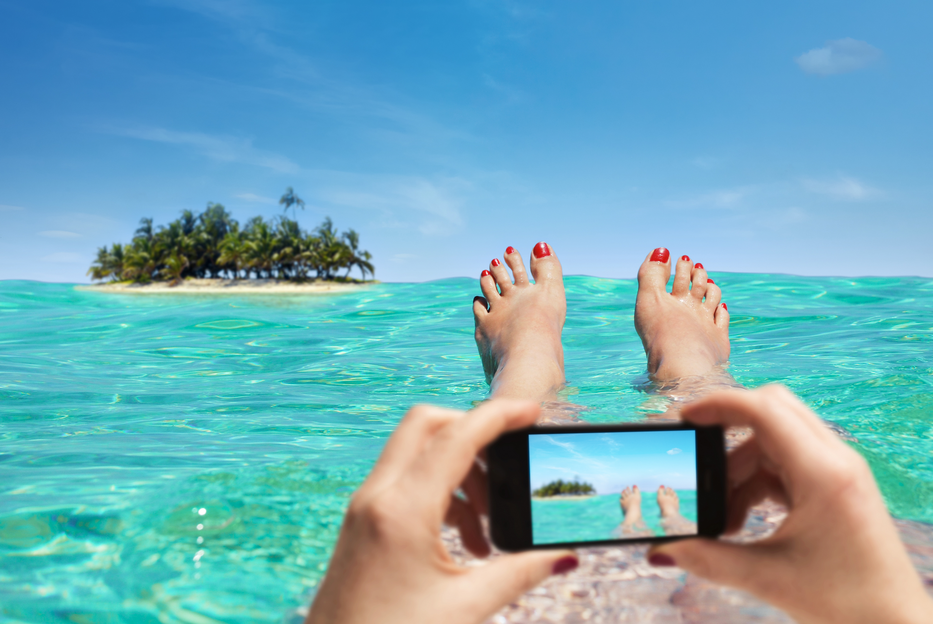 A person swims in the ocean while taking a photo on their phone