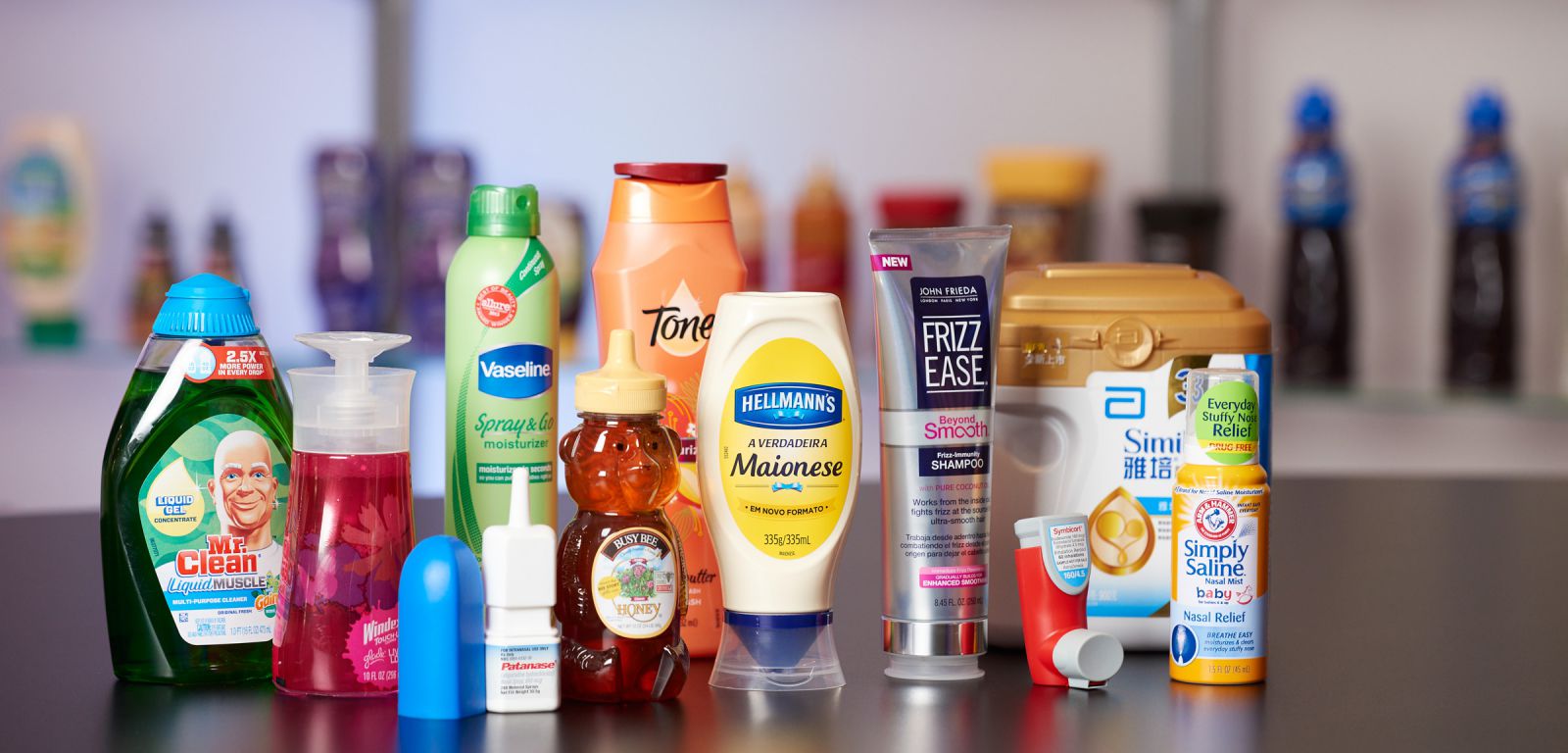 Various plastic containers from AptarGroup with products including soap, honey, mayonnaise, and eye drops.