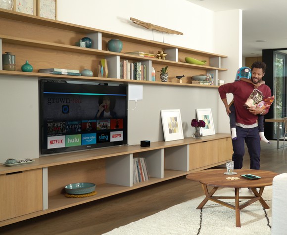 A man looking at a TV with an Alexa interface on display.