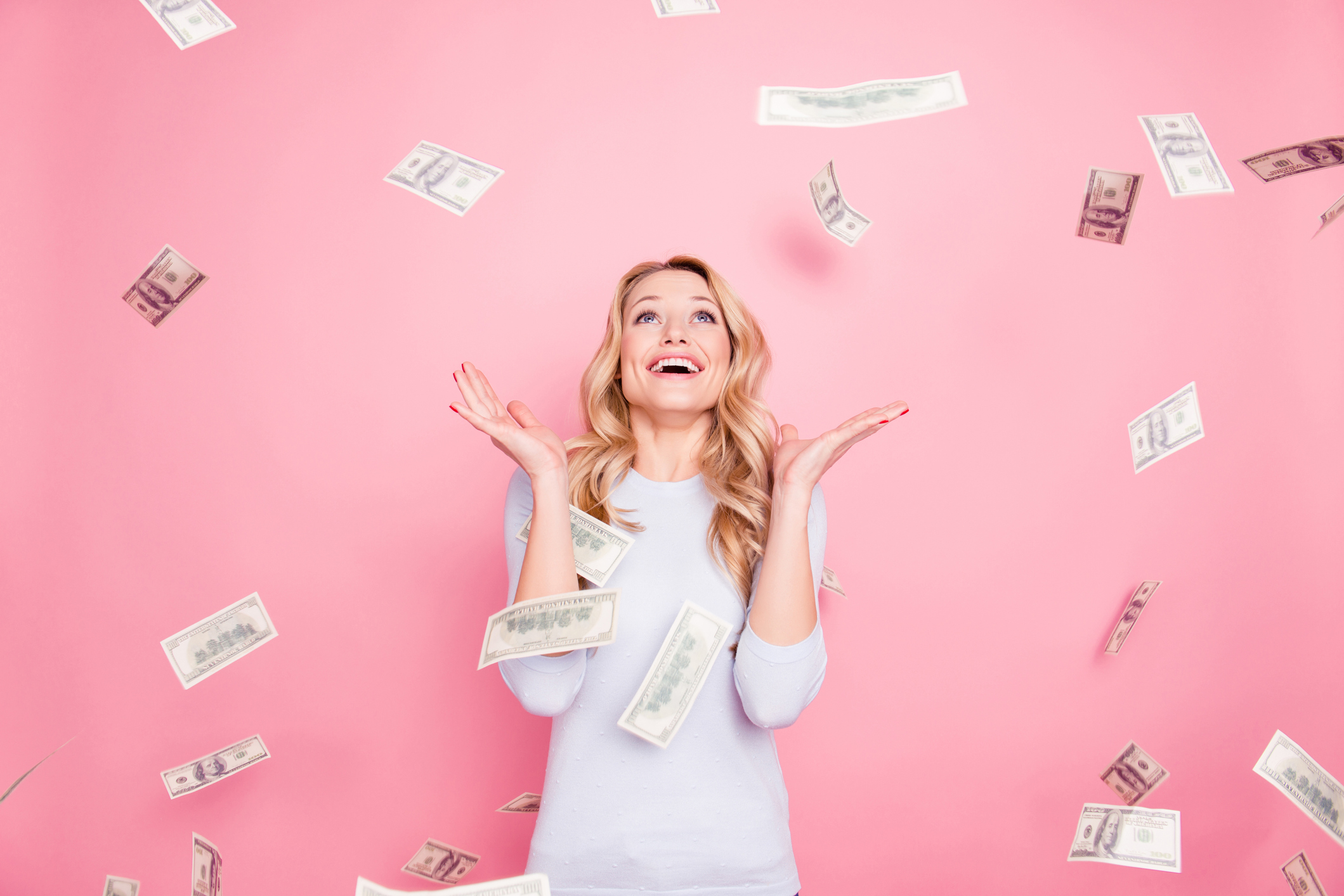 A woman looks up and smiles as hundred dollar bills rain down around her.
