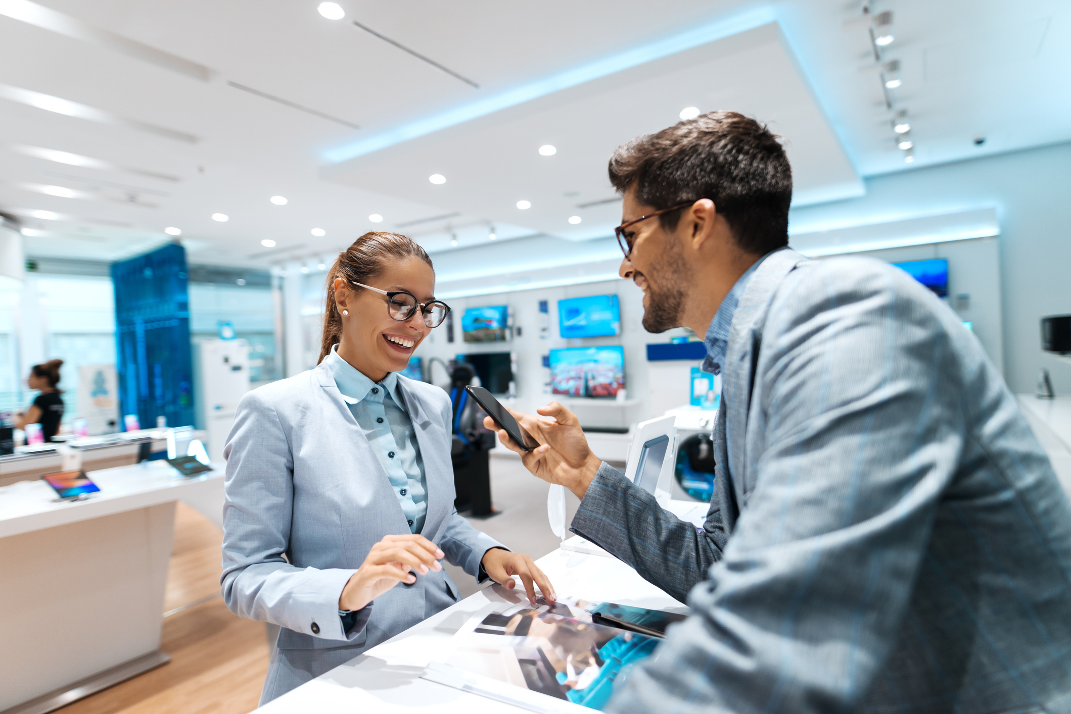 A man looking at a phone being shown to him by a female employee in an electronic store.
