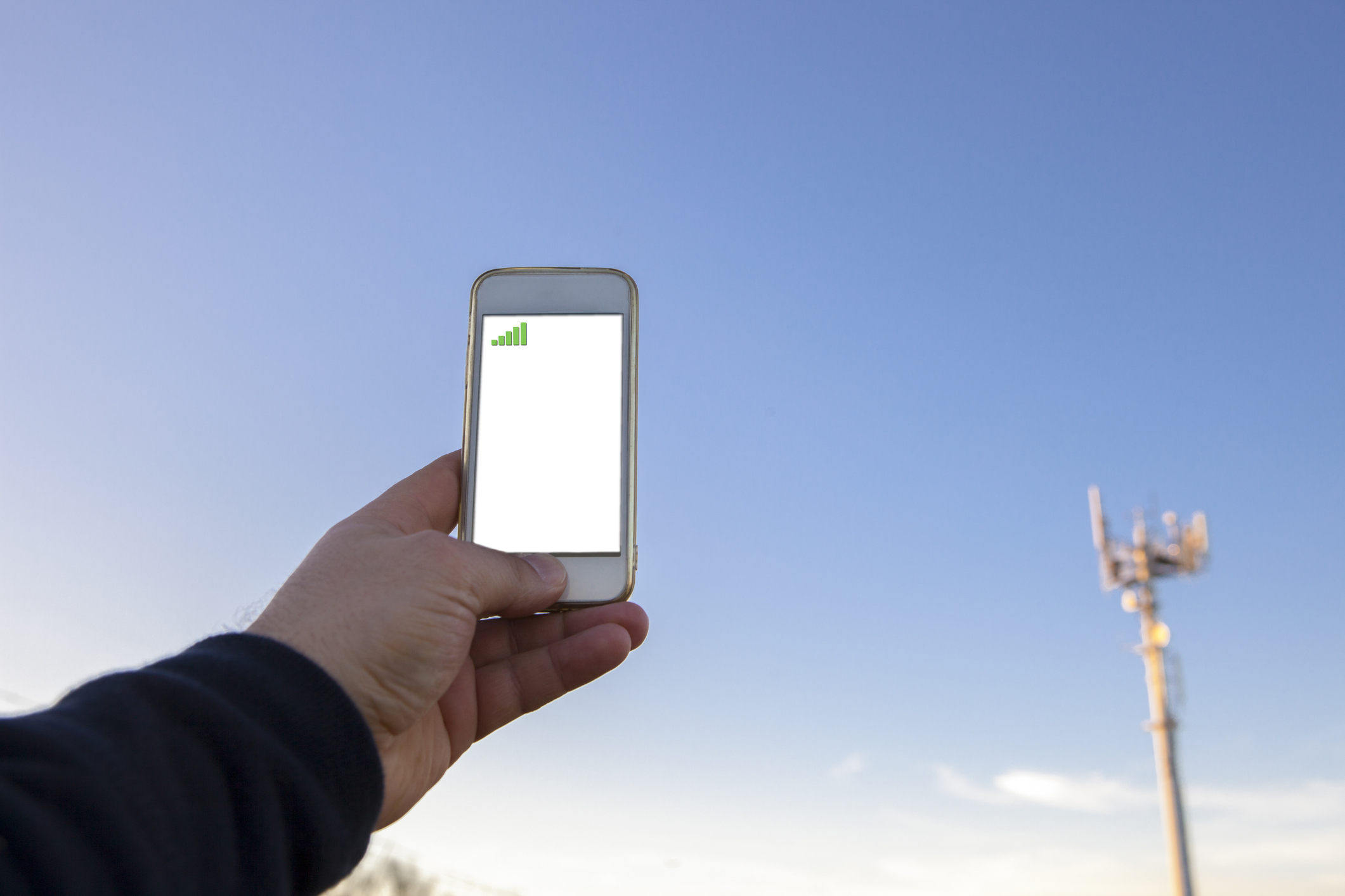 A man holds a smartphone up near a cellular tower.