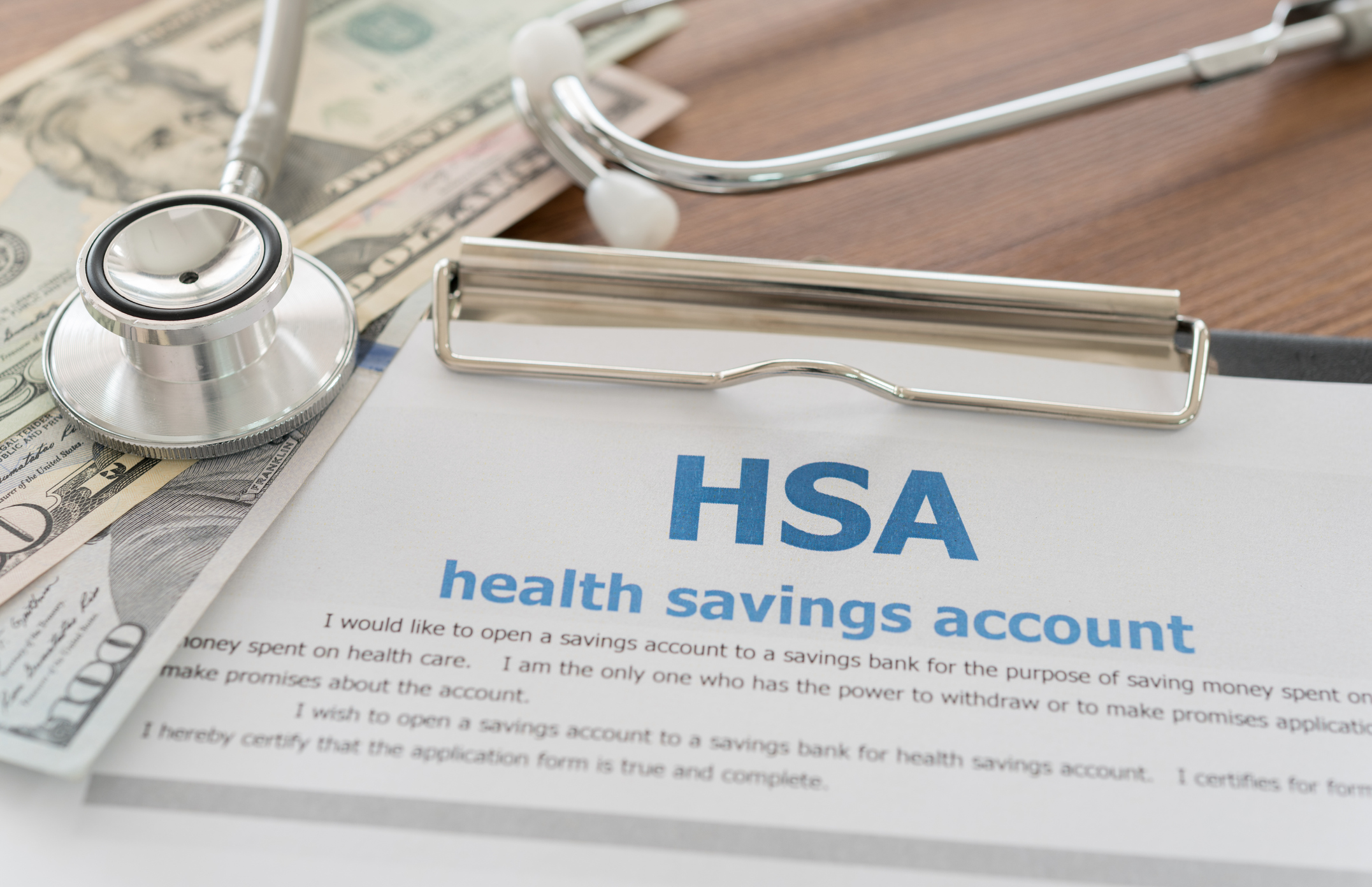 health savings account paper work on clip board with a stethoscope beside it and $100 dollar bills
