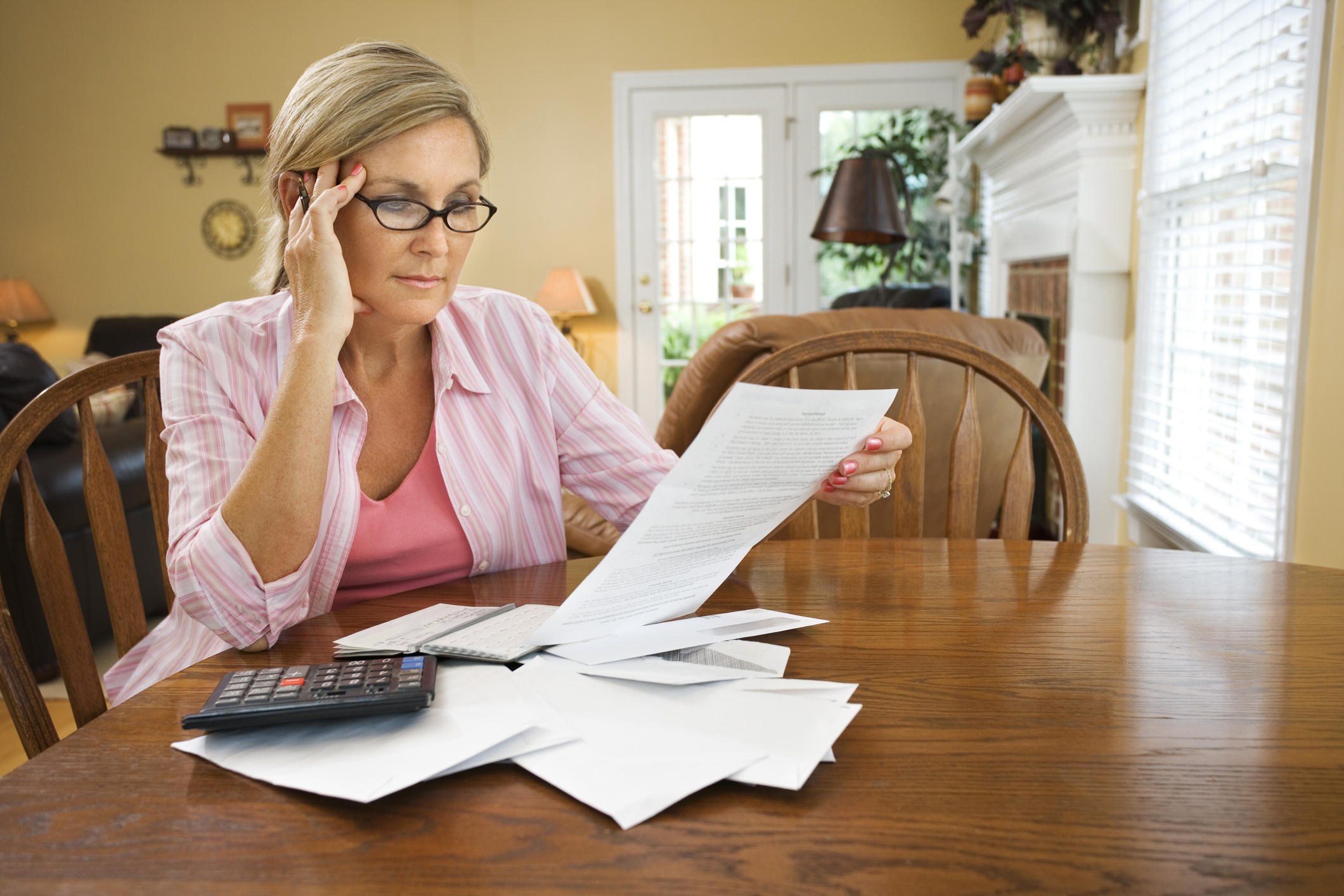 Woman looking at document; other papers are spread out on the table in front of her, along with a calculator