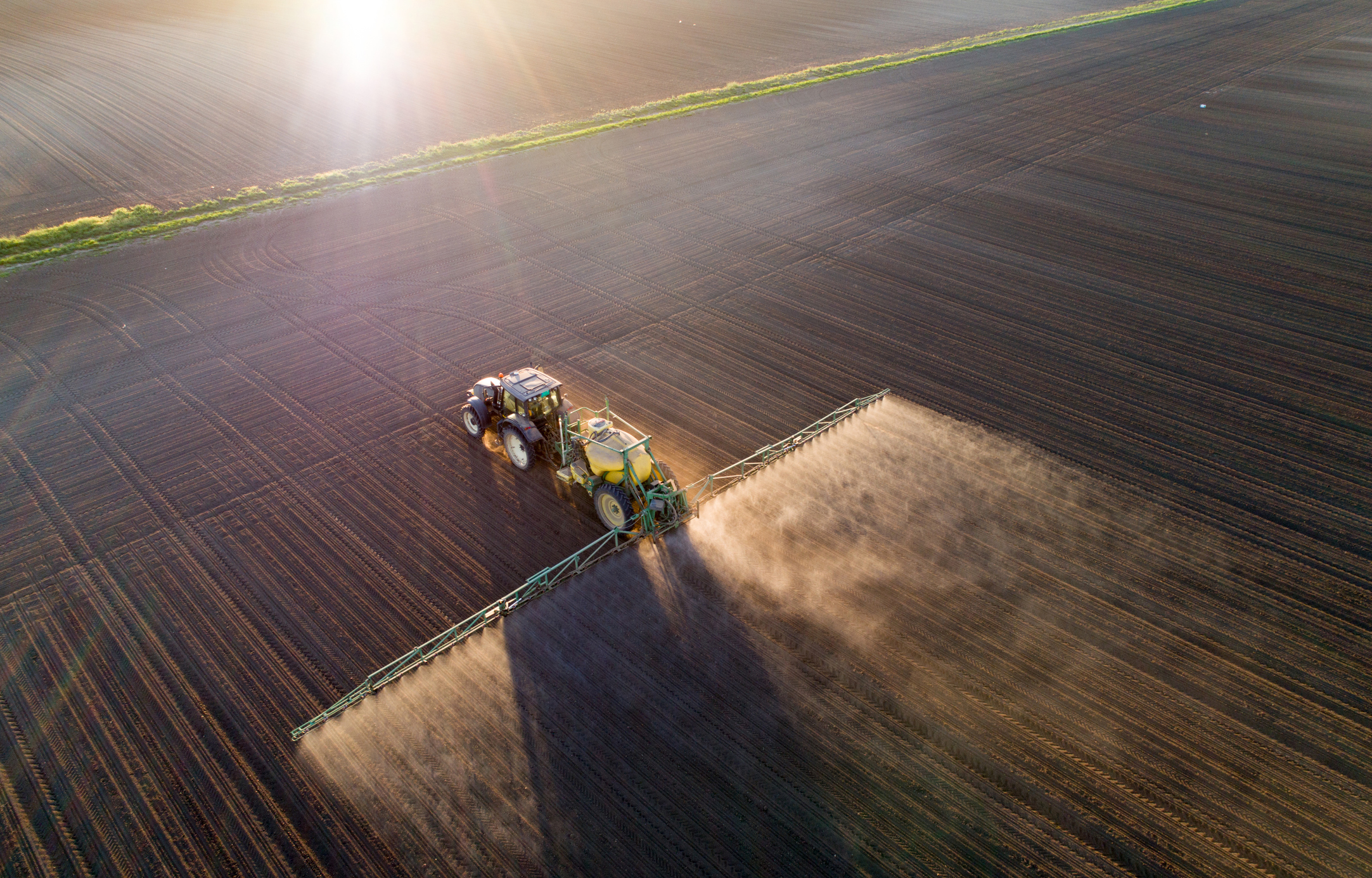 A tractor pulls a spraying machine through a field.