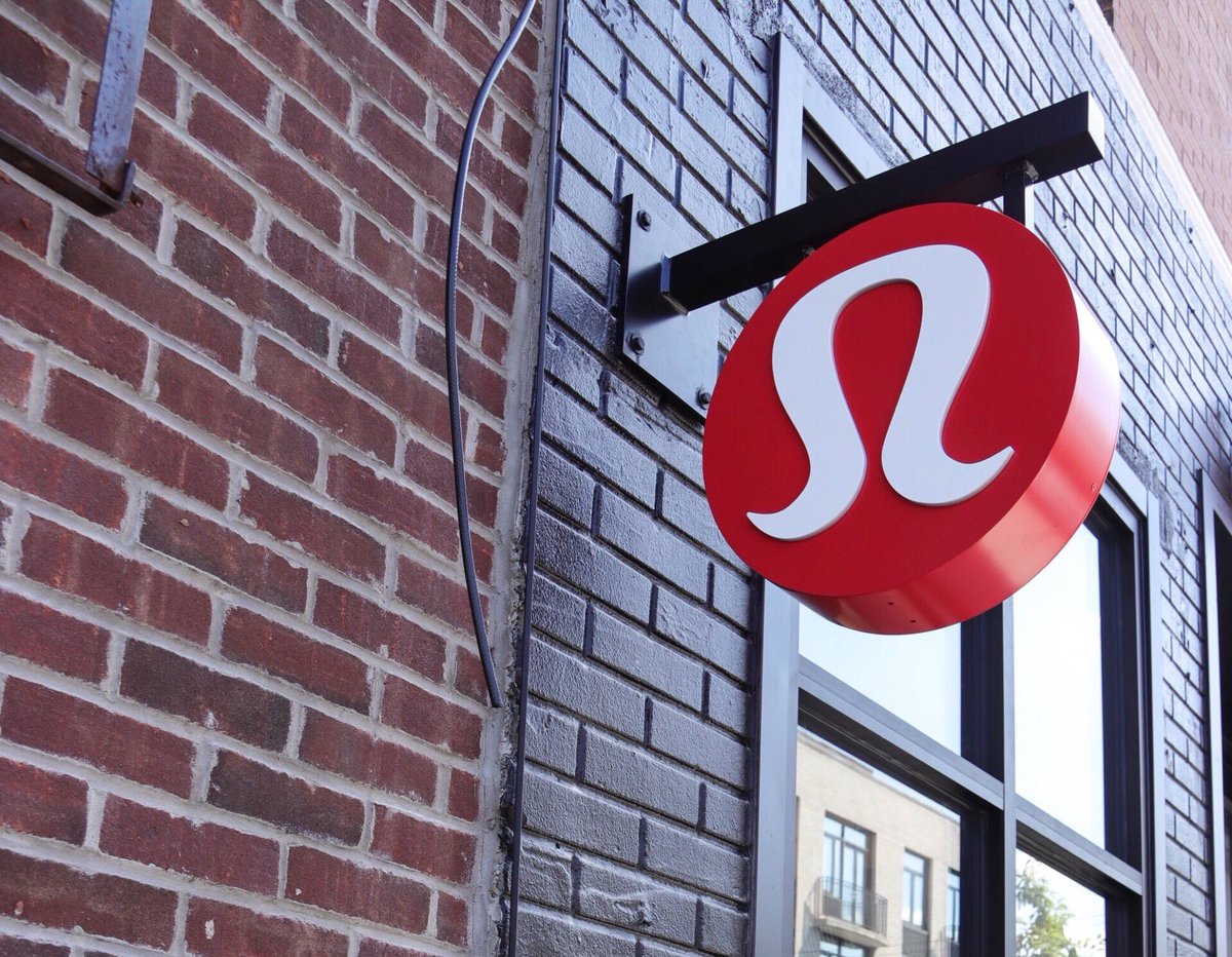Lululemon Athletica log hanging from a post near a window on the side of a brick building.