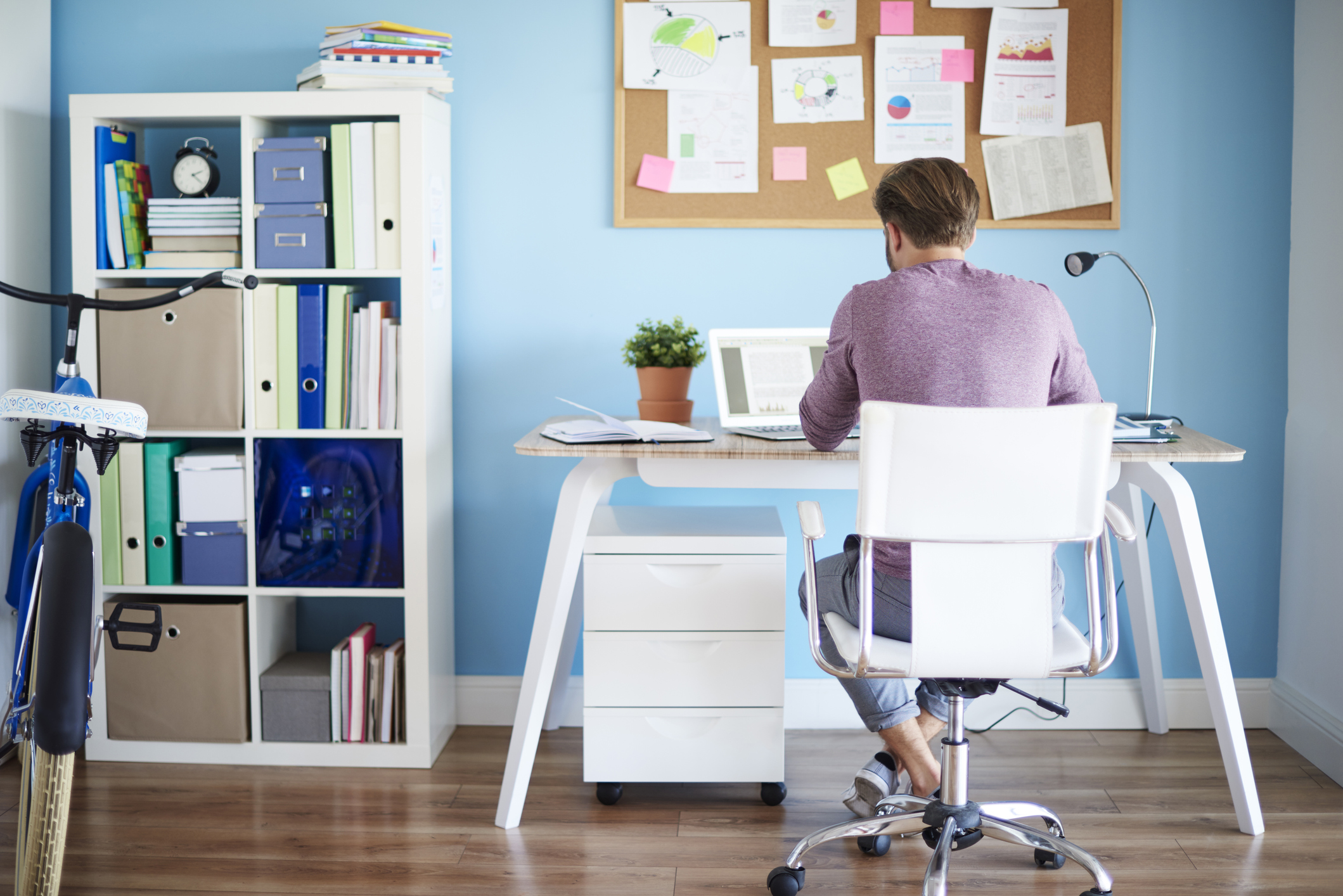 Man siting at desk in home office, facing a blue wall with a memo board