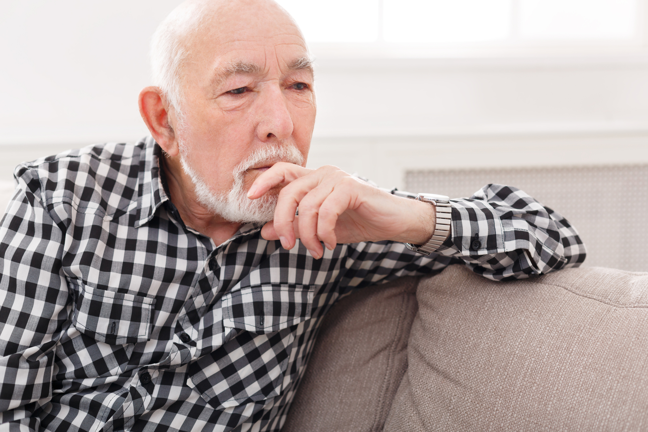 Older man sitting on couch with hand resting on chin.