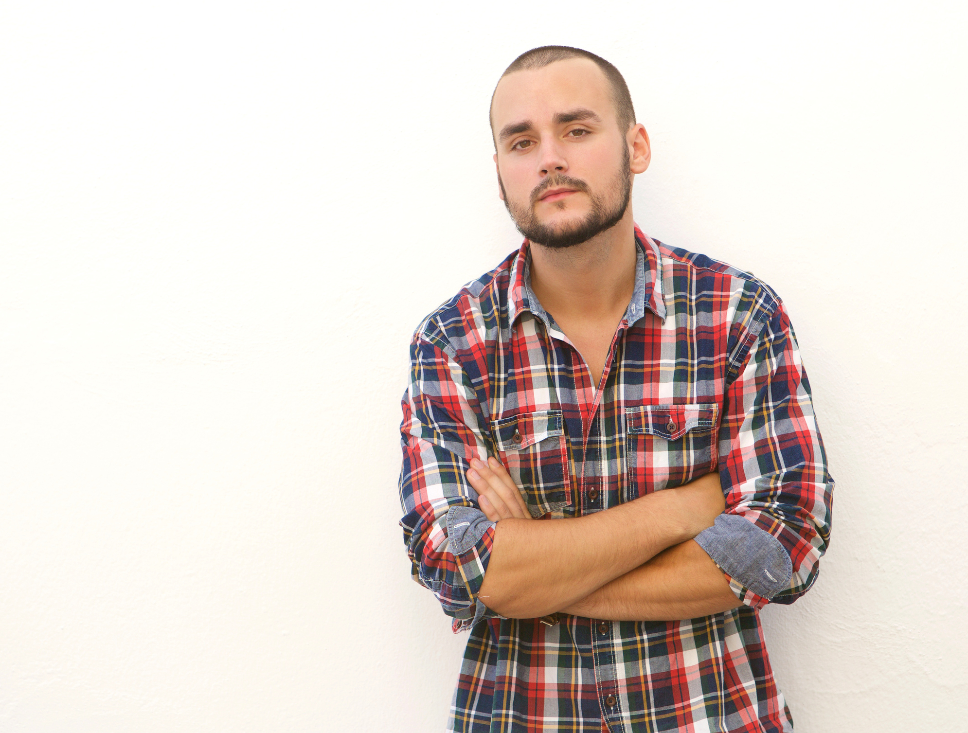 Young man in plaid shirt standing with arms crossed