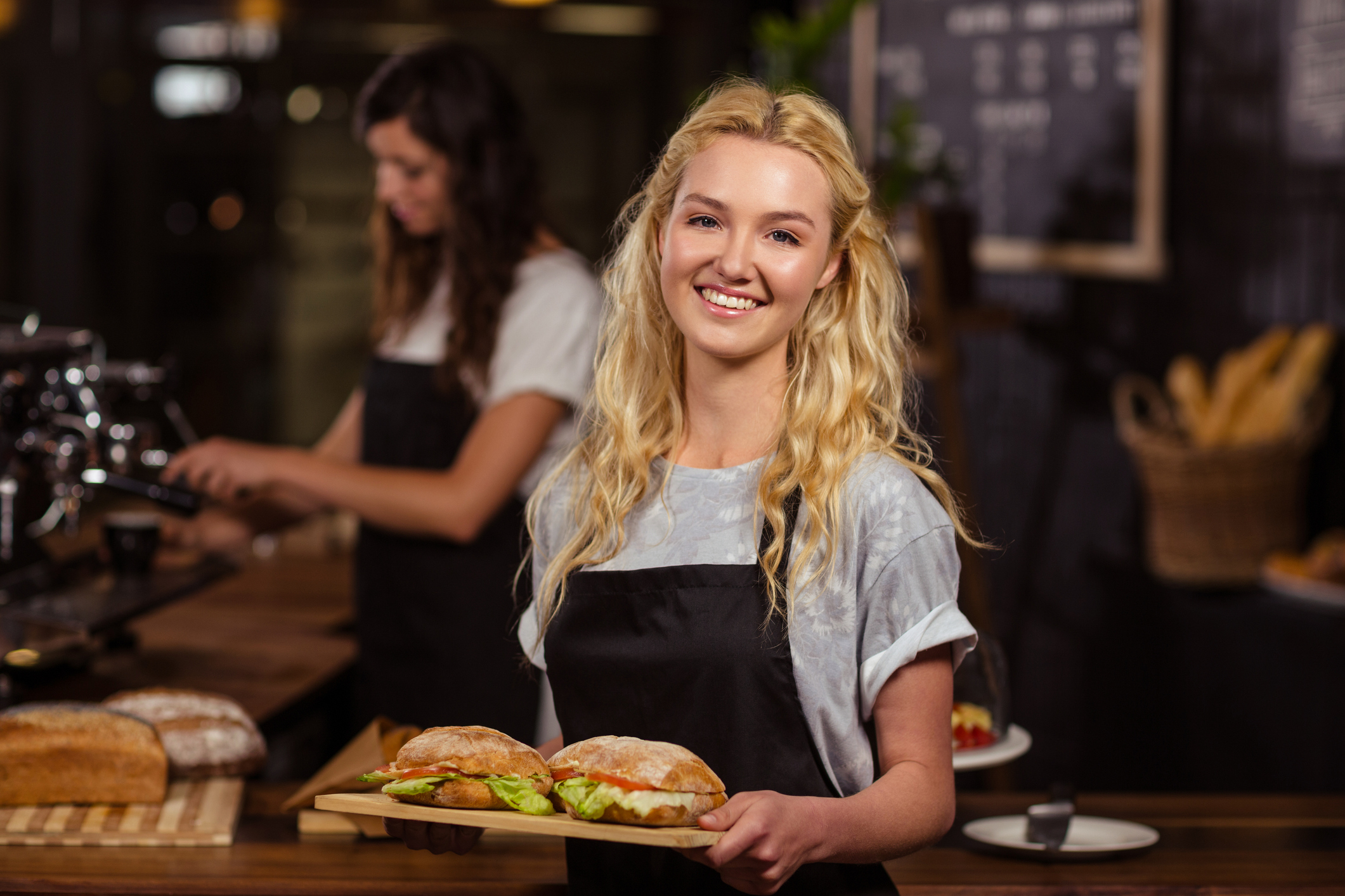 Smiling young woman in apron holding tray of food