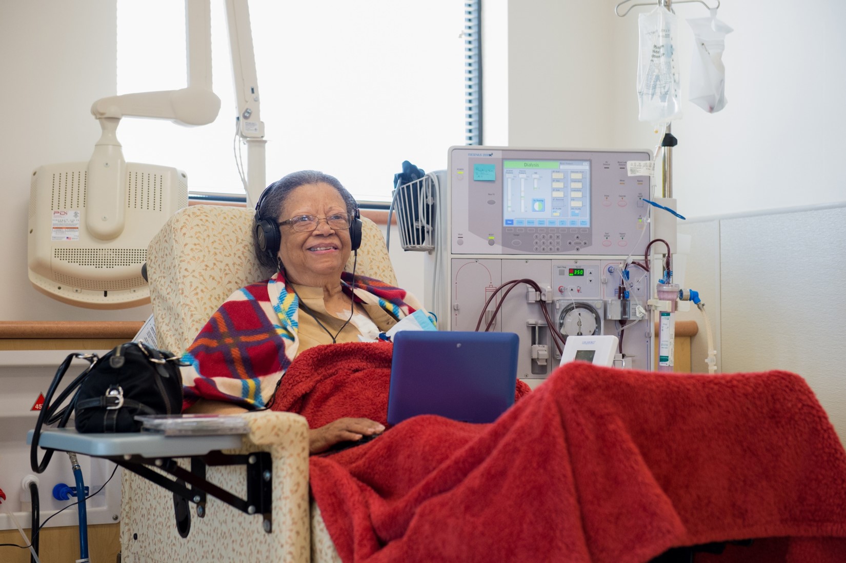 Woman reclining in an armchair and looking at a tablet, with medical equipment in background