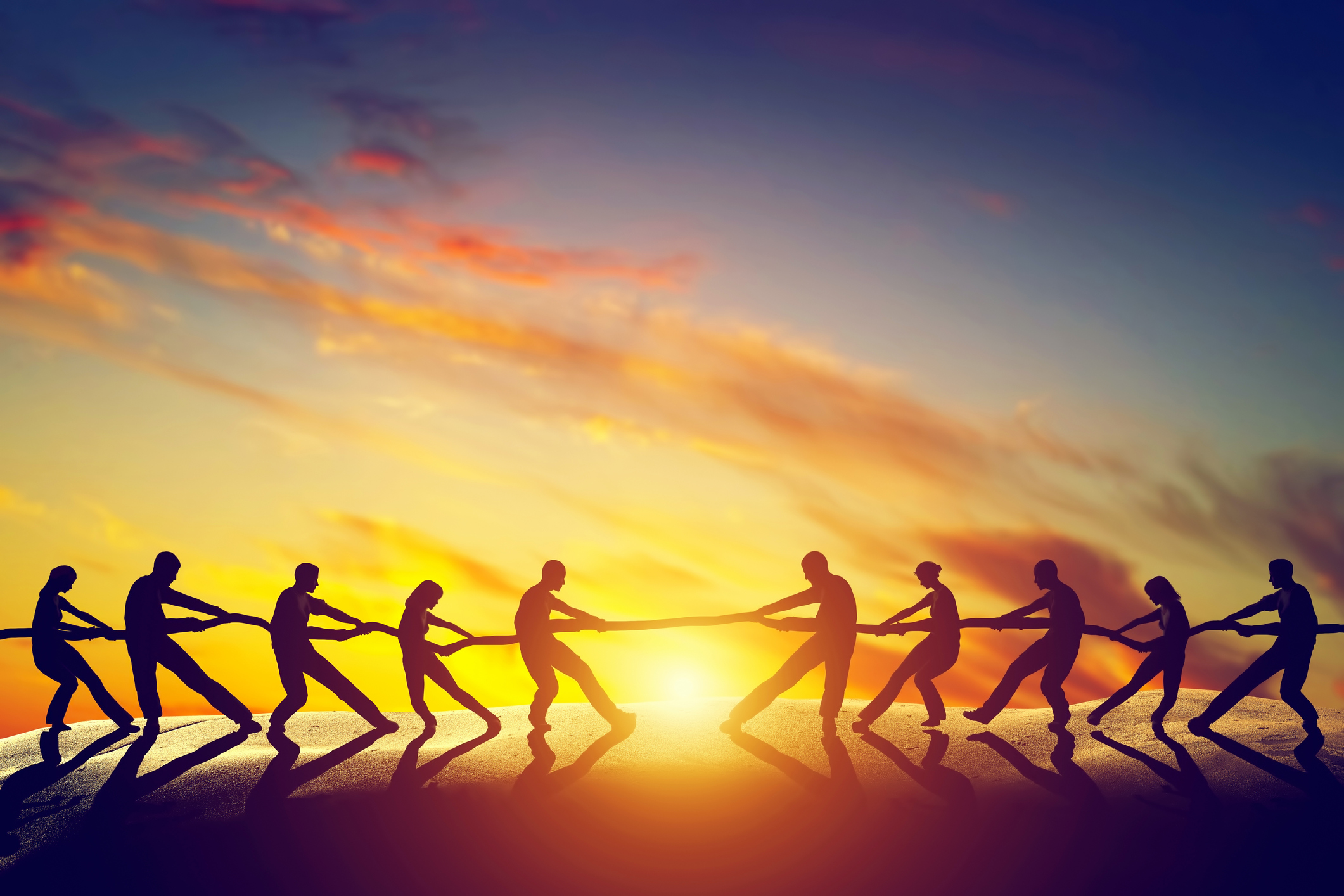 Two groups in a tug-of-war with the sun setting in the background.