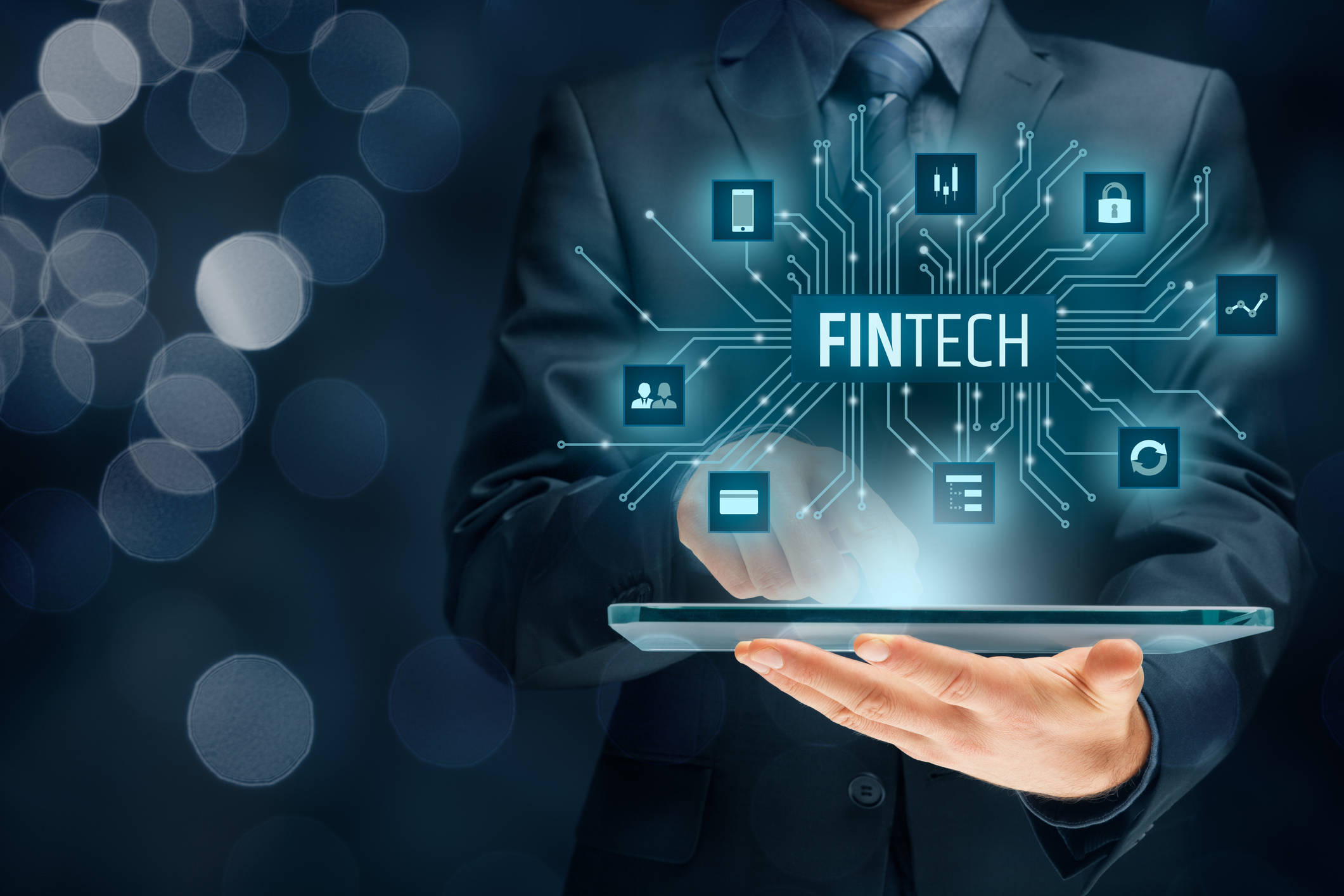 The word Fintech pops out of a tablet held by a man in a suit viewed from the neck-down.