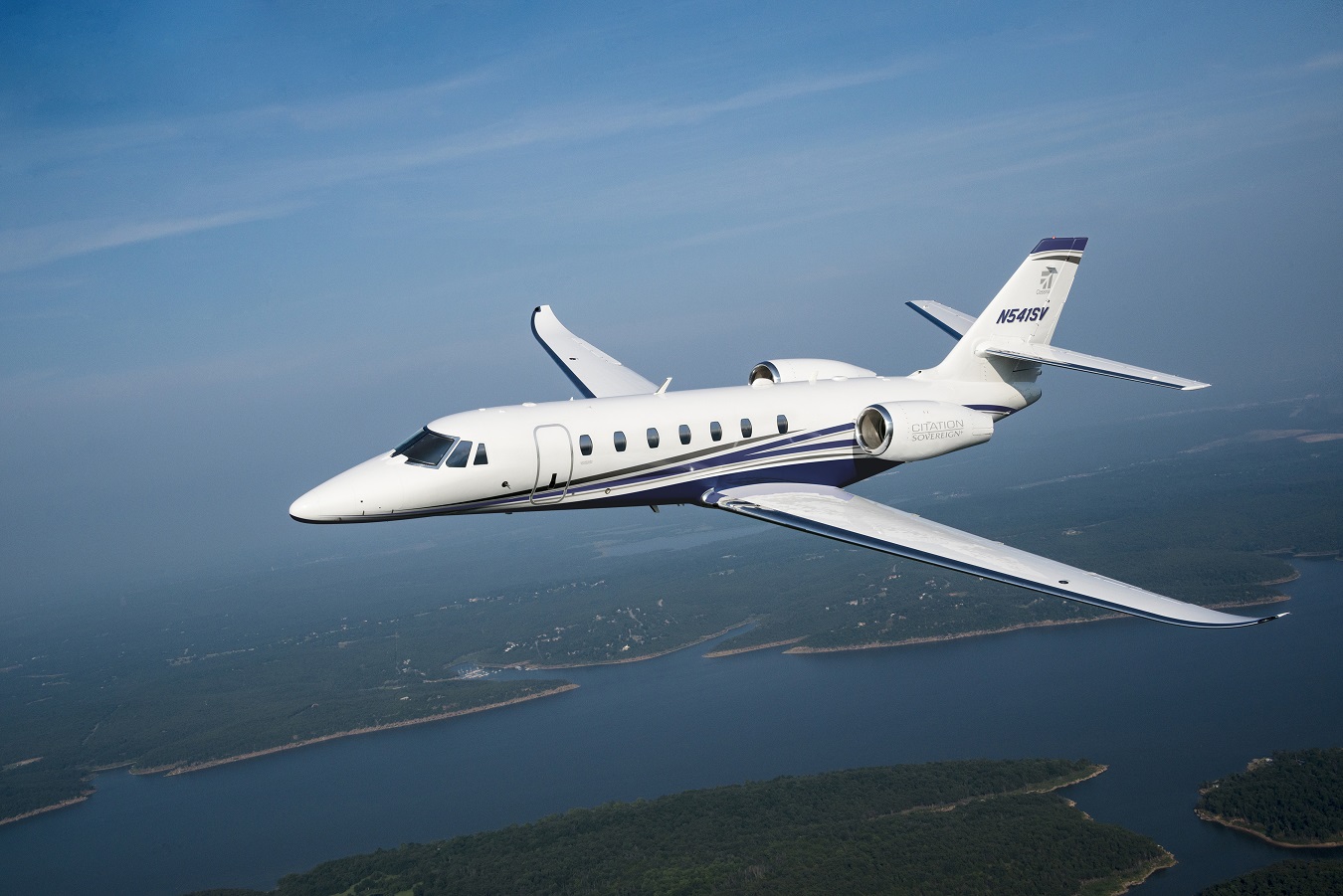 Cessna Sovereign jet in flight over a lake.