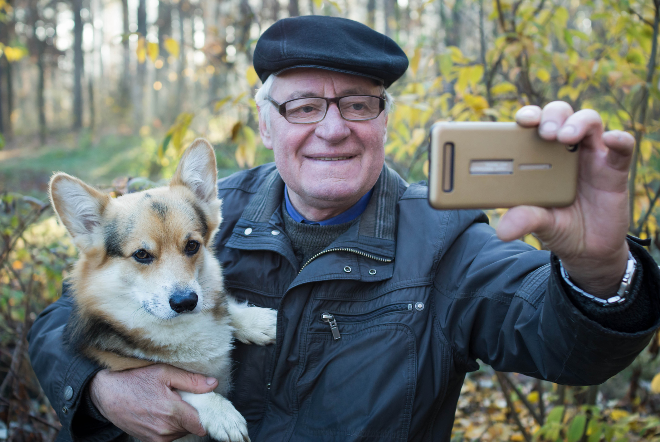 Older man outdoors holding dog and taking selfie
