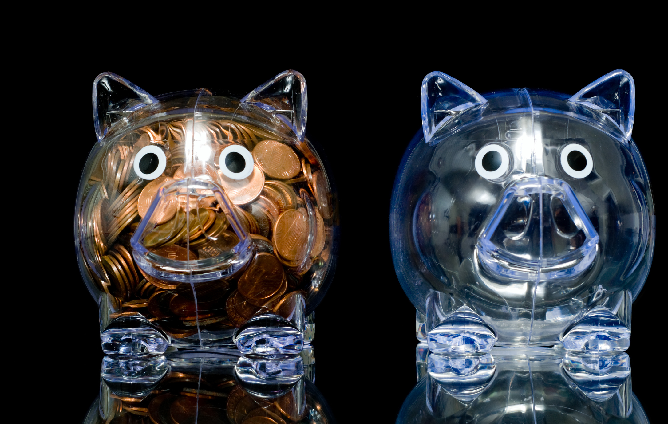 Two transparent piggy banks, one full of pennies and the other empty