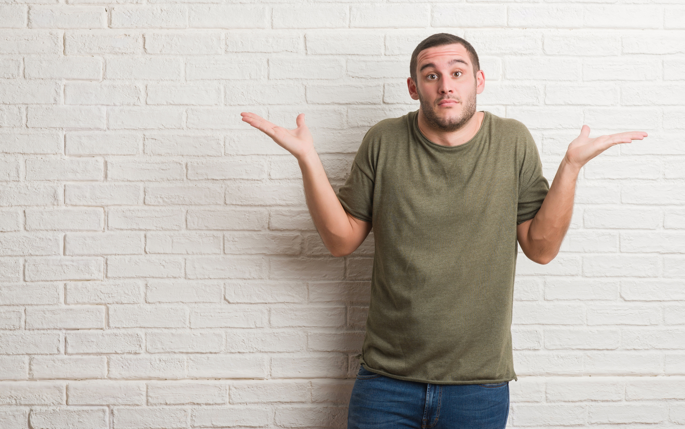 Man standing against a brick wall, shrugging