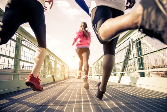 A picture from the ground up of three young people wearing sports gear and running across a bridge.