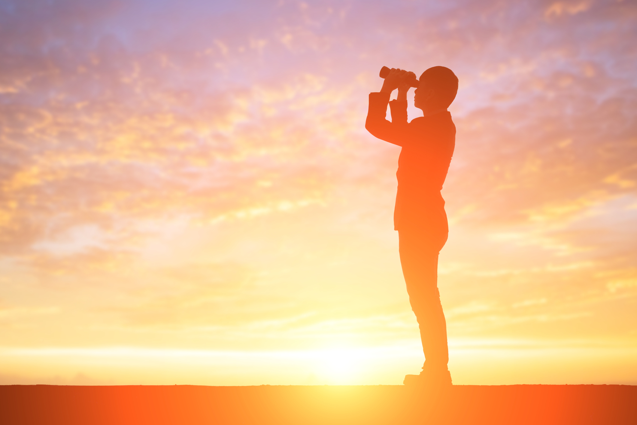 A person looking through binoculars at sunset, silhouetted against a golden sky