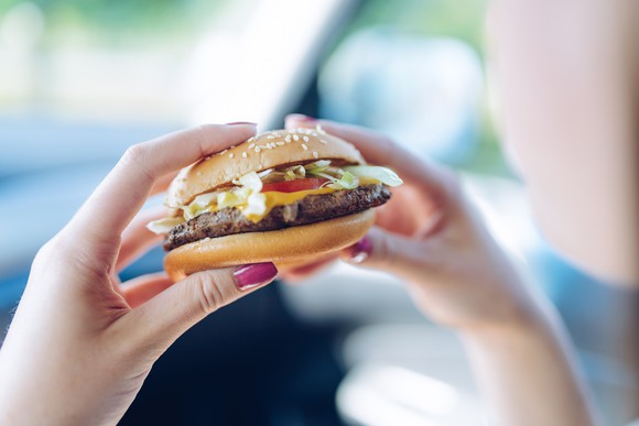 A hamburger being held by someone sitting in a car