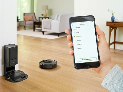 A person uses a smartphone to program a Roomba i7.