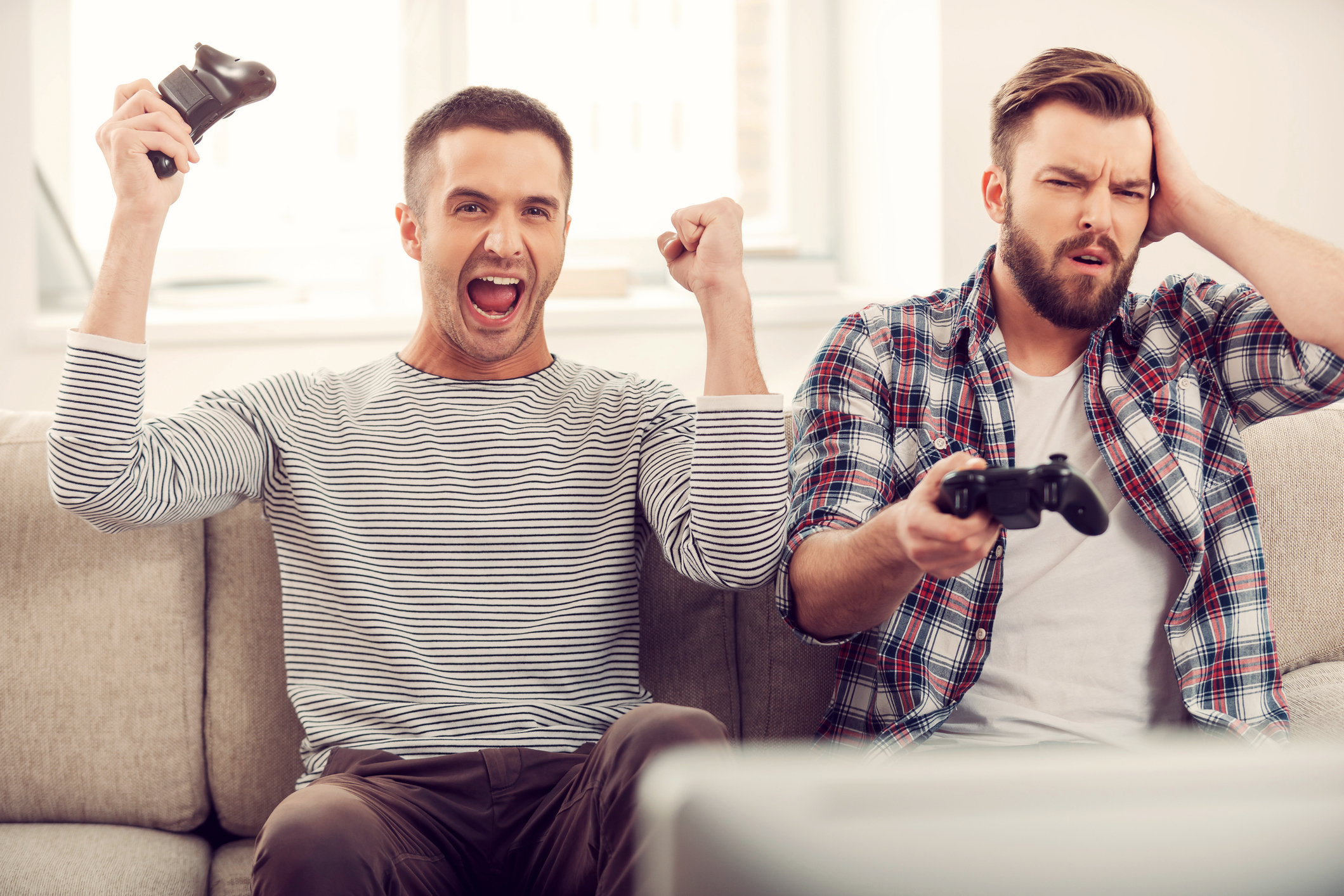 Two men playing video games with one happy and one disappointed.