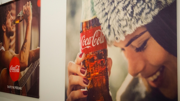 An ad for coke with a young woman holding a coke bottle to her forehead and smiling.