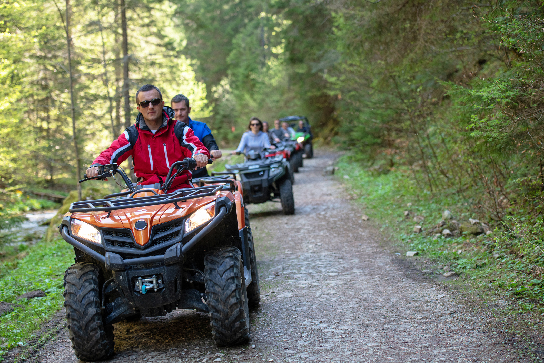 A group of people riding all-terrain vehicles down a narrow path in the forest.