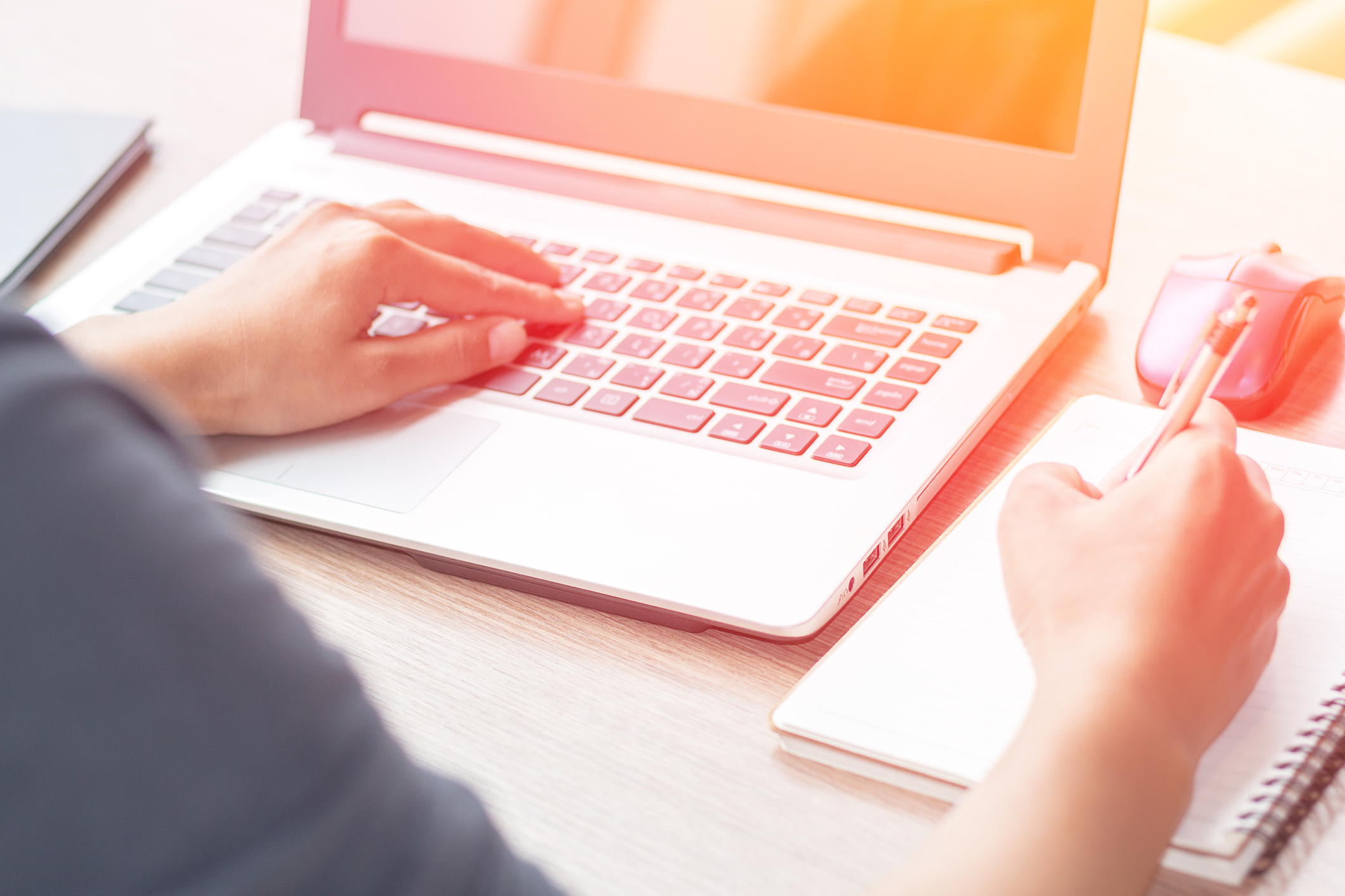 Woman typing on a laptop and taking notes