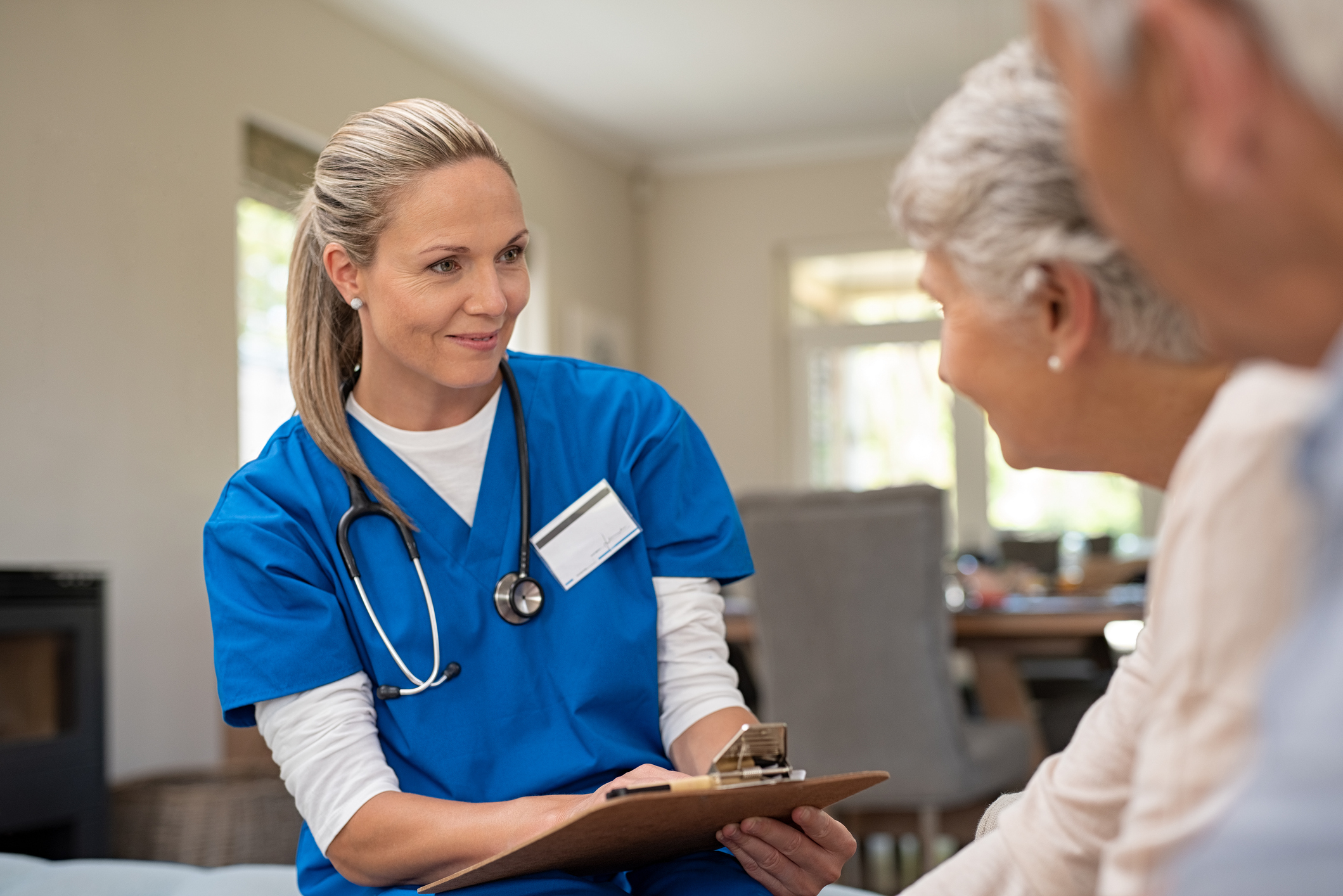 A woman in hospital scrubs with a stethoscope around her neck speaking with a gray-haired couple.