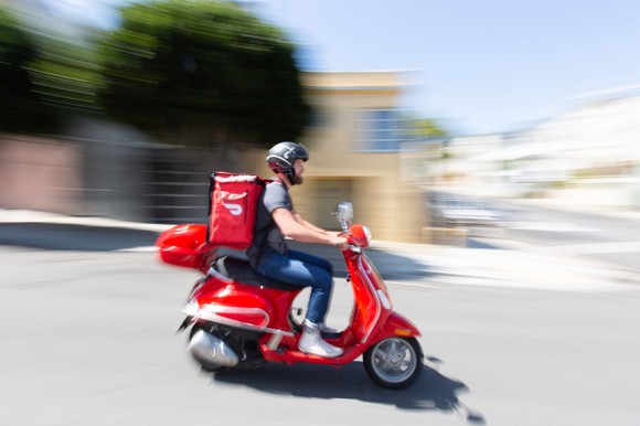 A DoorDash delivery person is seen riding a moped to deliver a product.