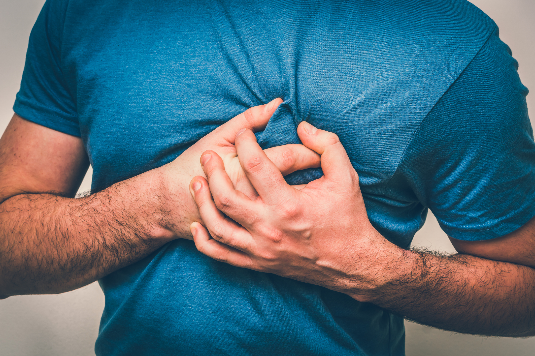 A man in a blue shirt appearing to clutch at his heart with both hands.