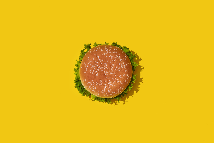 A overhead view of a burger sitting on a yellow surface.
