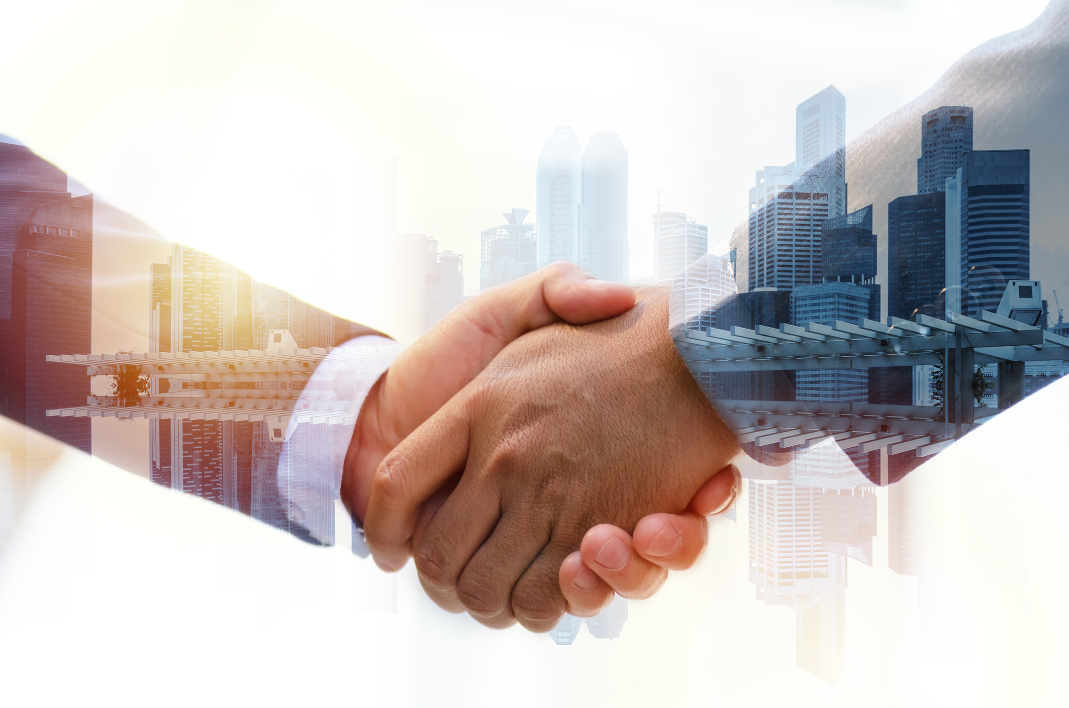 Two people shaking hands with office buildings in the background.