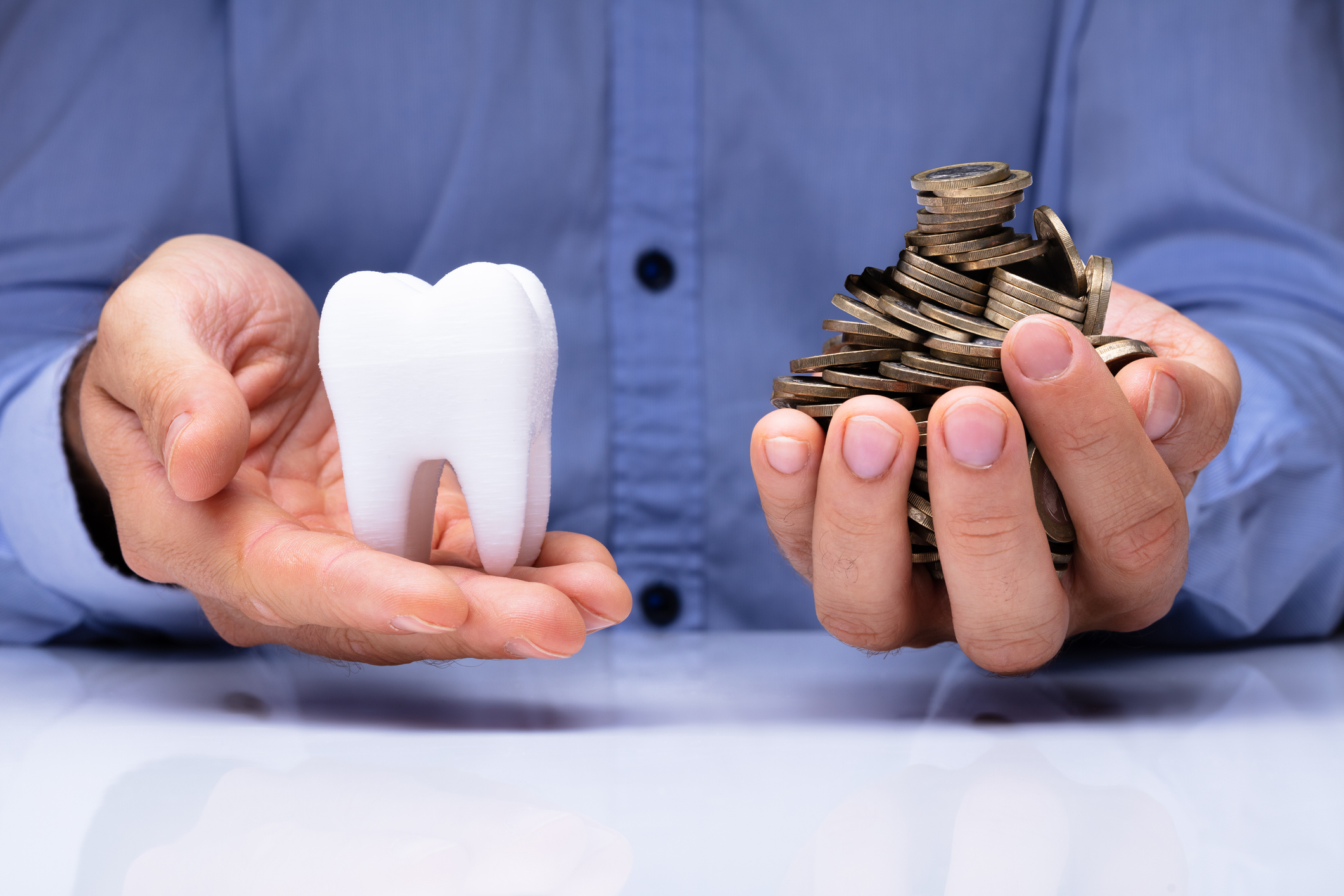 Man holding a large tooth model in one hand and a pile of coins in the other hand