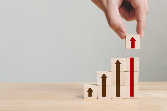 A hand placing a block onto a column of blocks with an upward facing arrow on their faces.