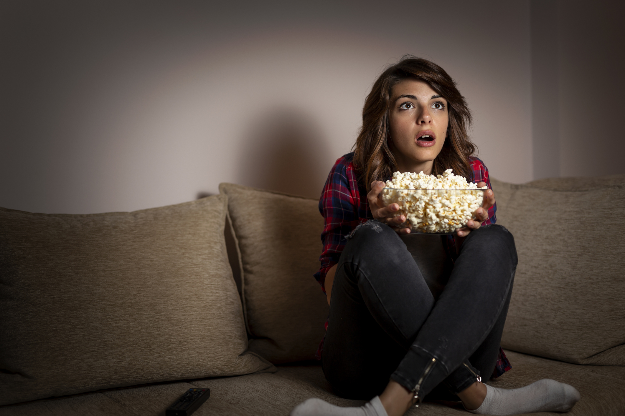 A girl sitting on a couch with a bowl of popcorn.