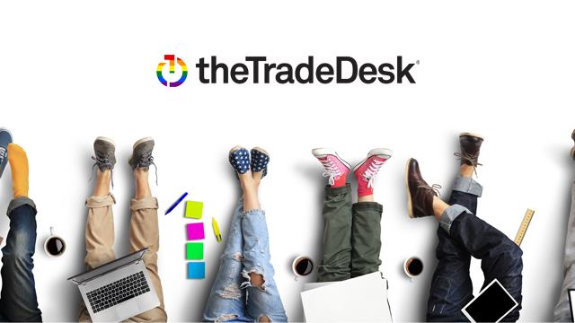 Several legs and feet of people with laptops, on a graphic bearing The Trade Desk's logo