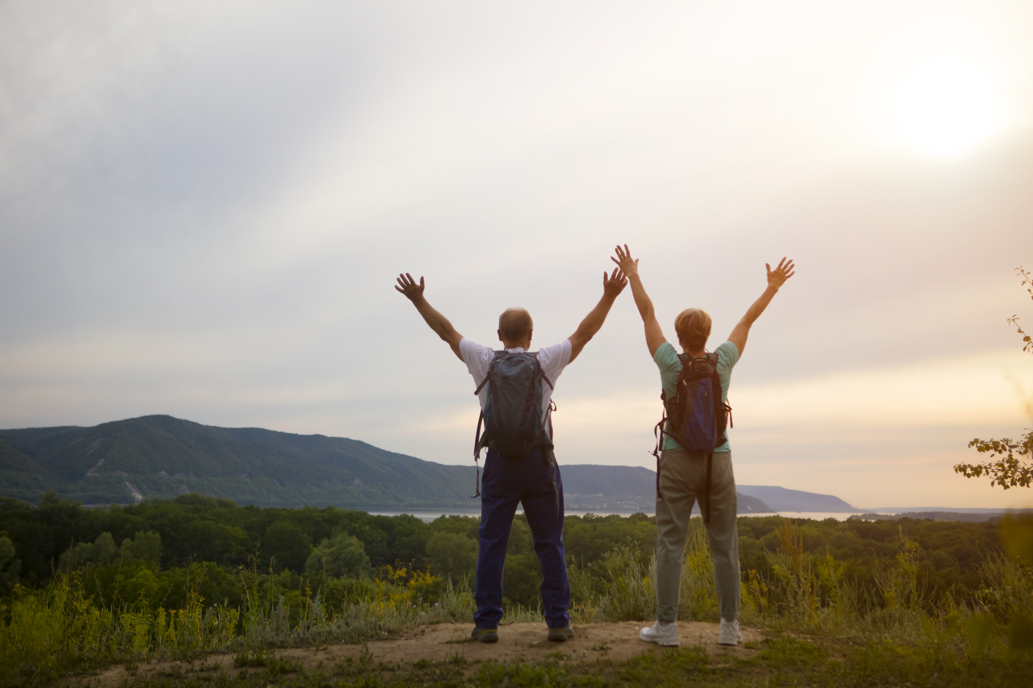 Two hikers standing at a vista with their arms outstretched above their heads