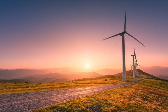 Wind turbines along a road with the sun setting in the background.