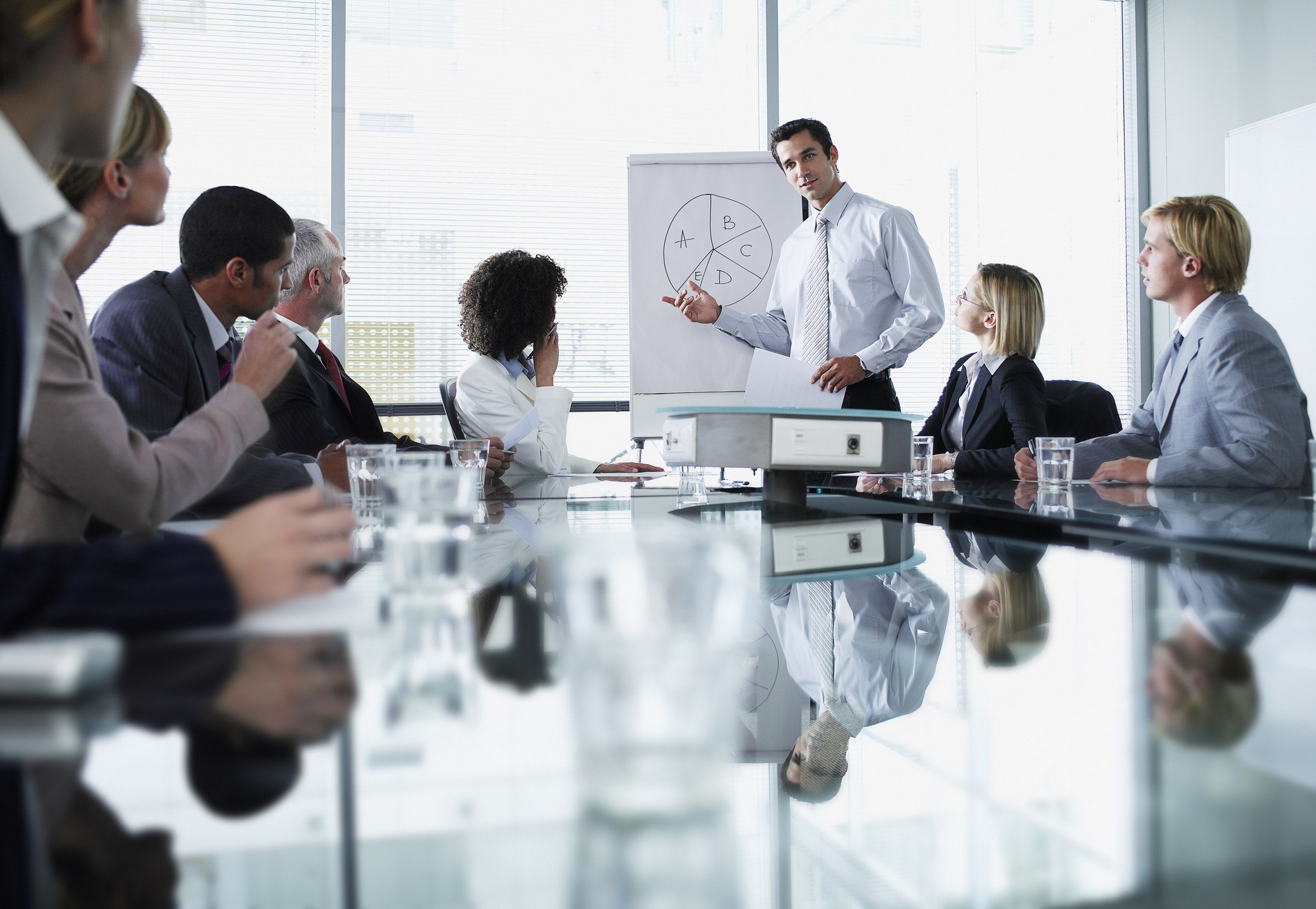 A man leads a presentation around a table in an office setting.