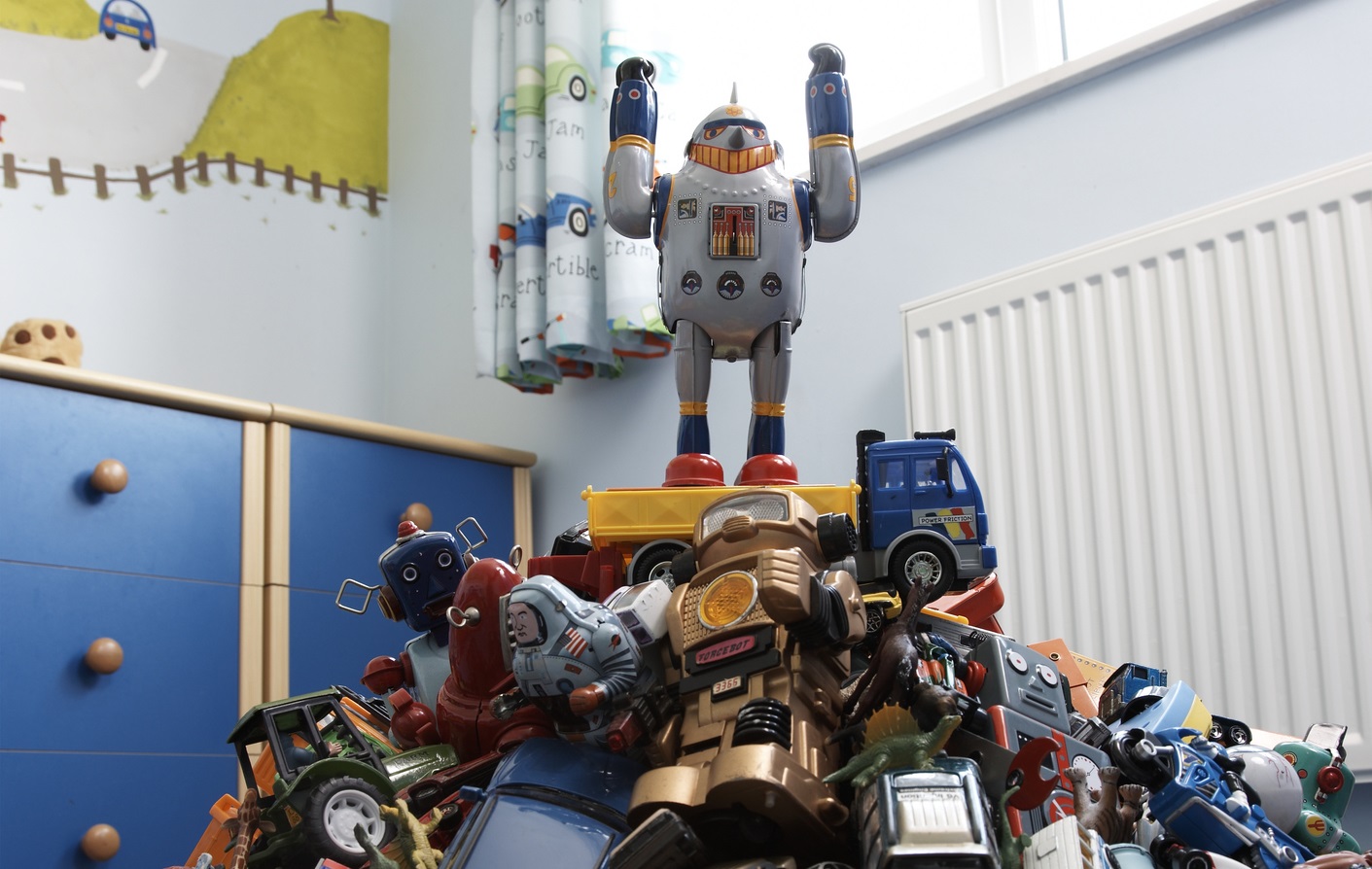 A toy robot stands on top of a pile of toys, its arms raised.