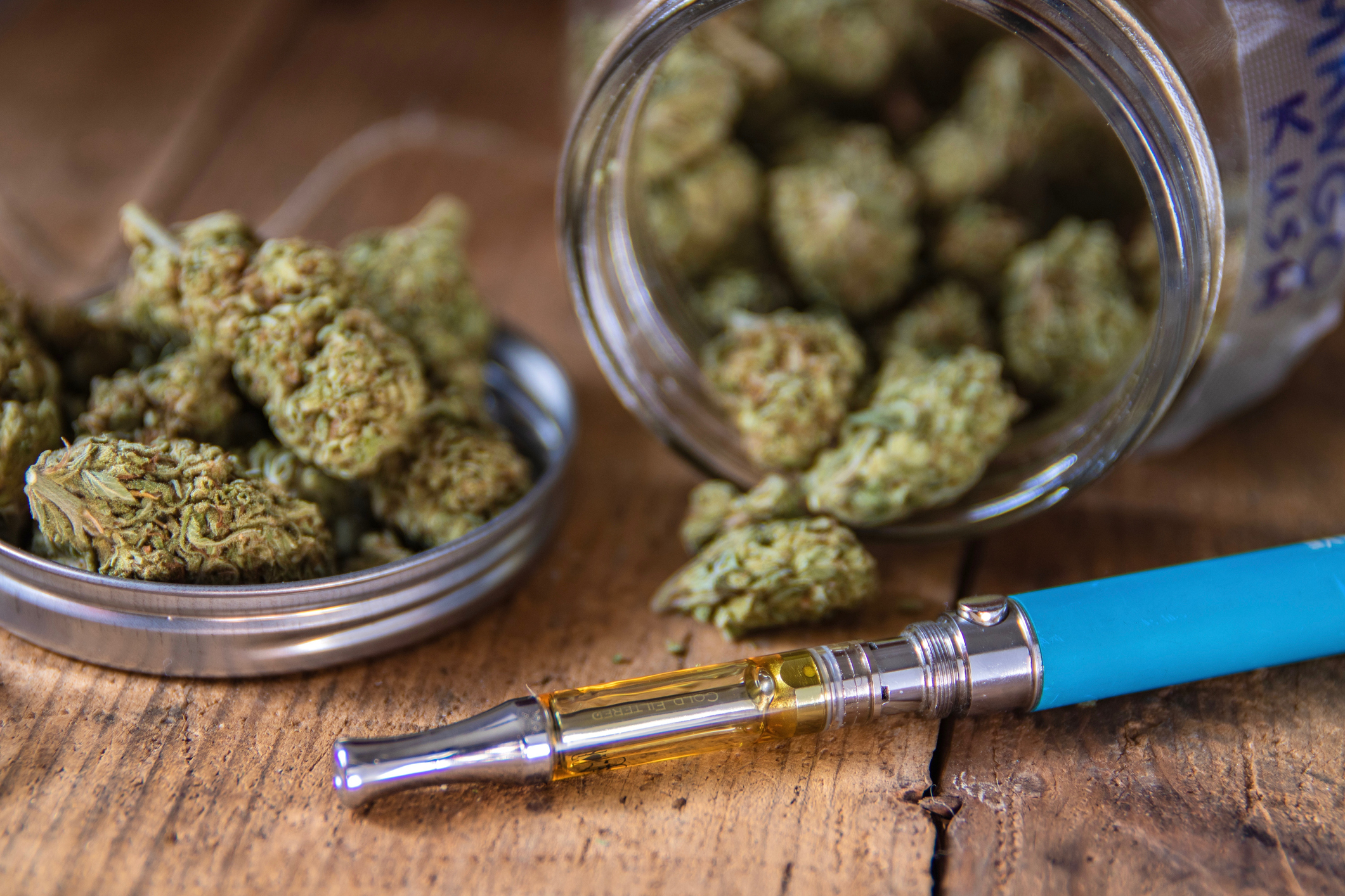 Cannabis buds in an overturned glass jar next to a vape pen