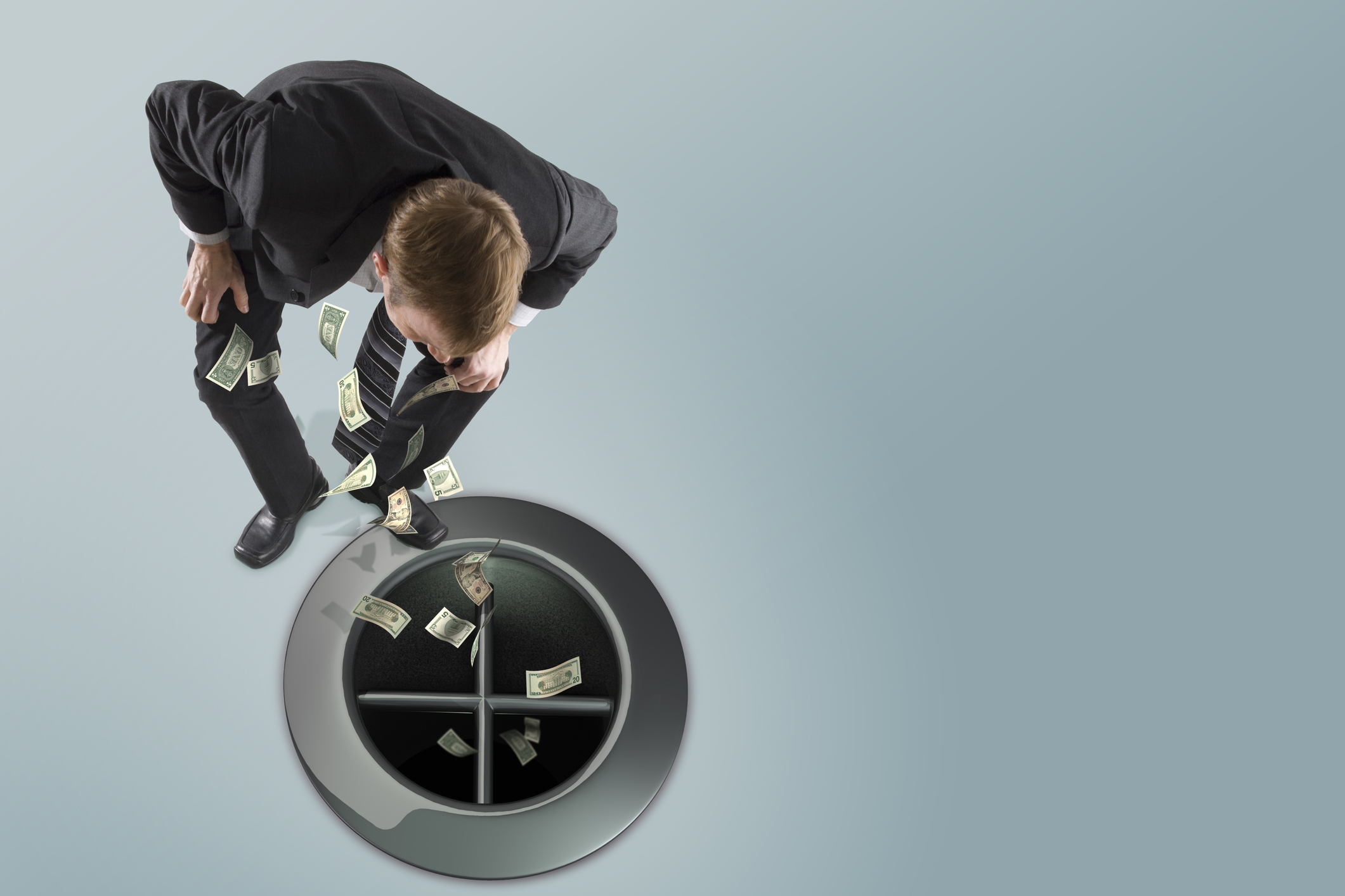 Businessman watching money go down a giant drain.